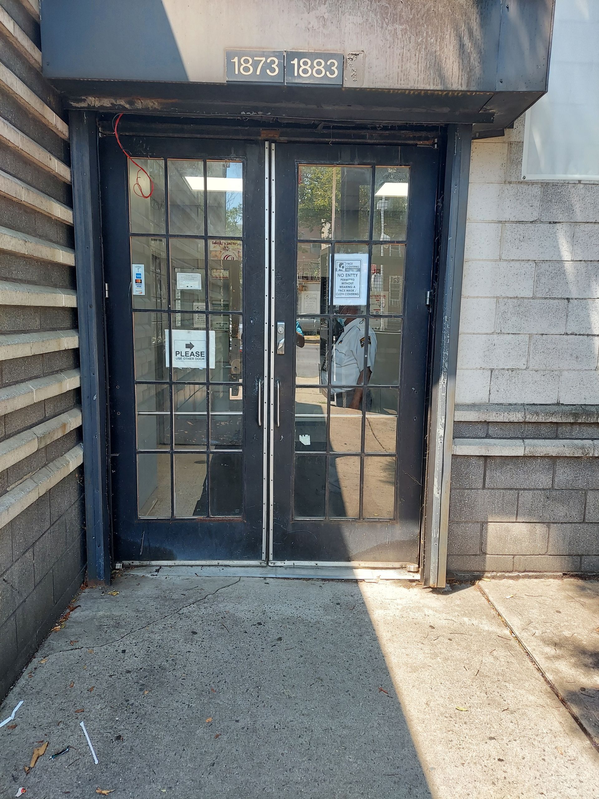 Glass double doors at 1873-1883 with posted notices and a sunlit concrete entrance.