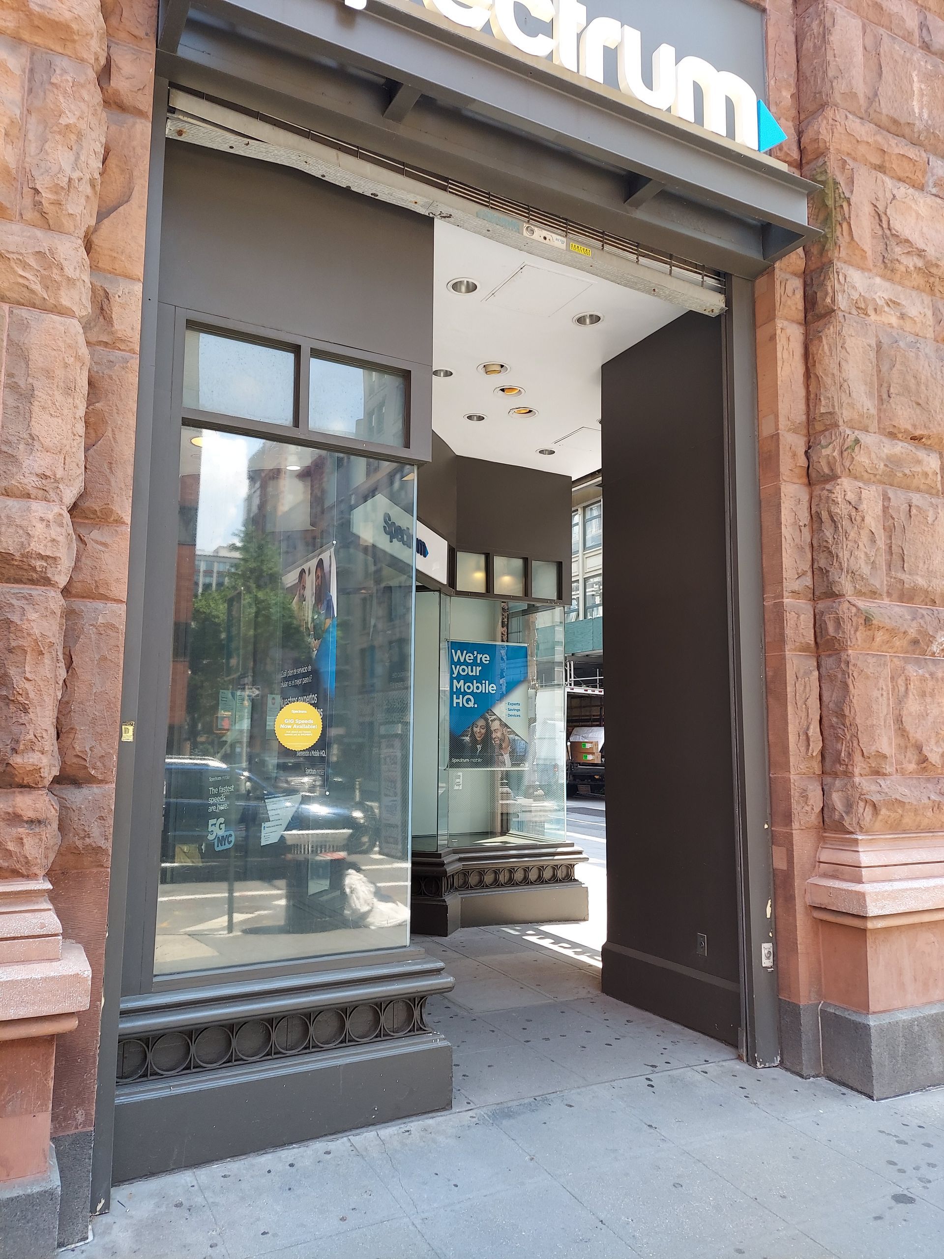Storefront entrance with open door, glass display window, and stone facade on a sidewalk.