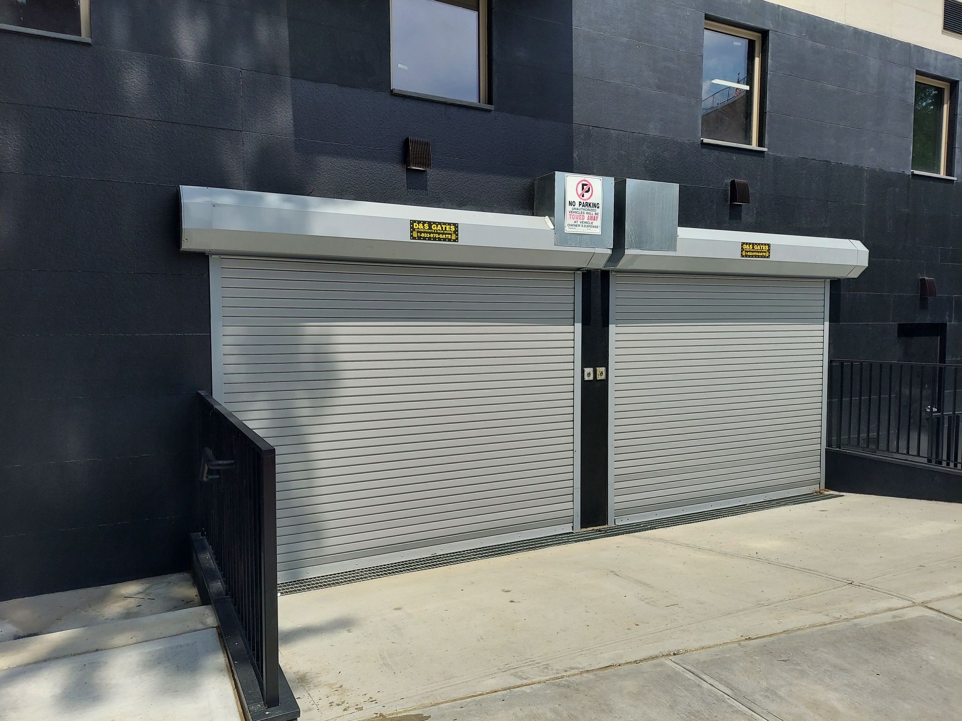 Two closed metal roll-up doors on a dark building exterior, with a small sign above each.