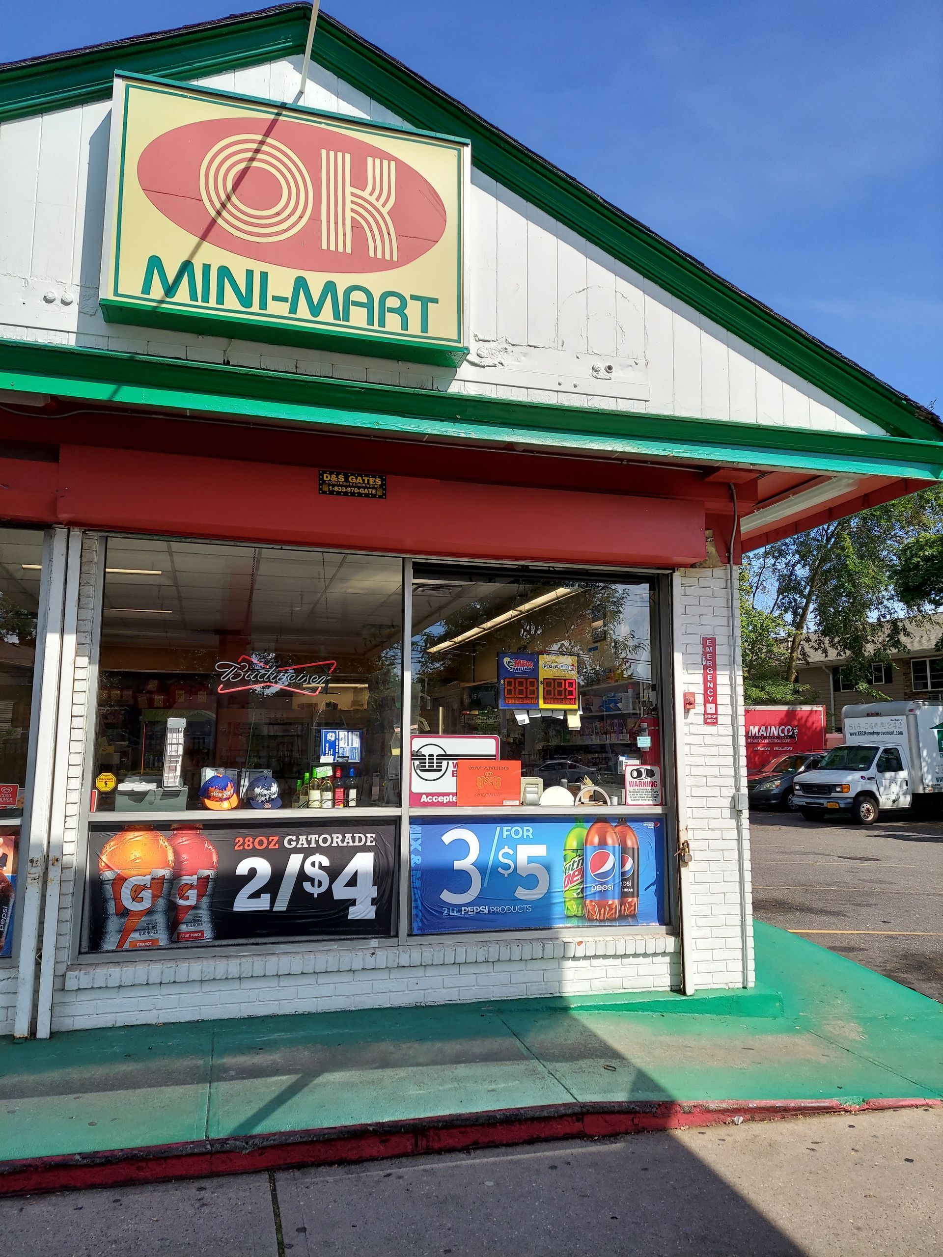 Mini-mart storefront with red trim, green roof, and colorful sale signs by the entrance.