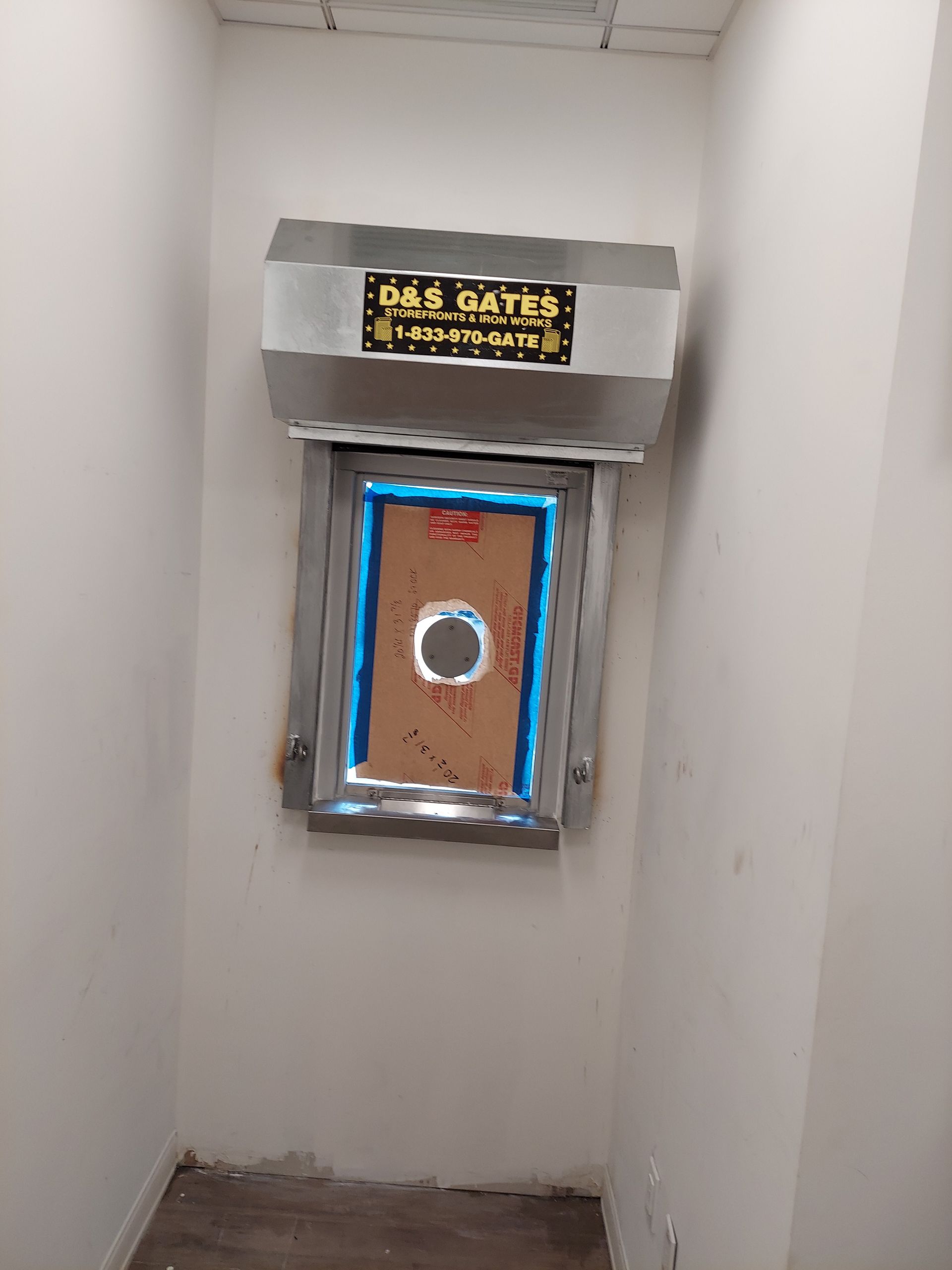 Narrow white hallway with a small boarded window and a sign above it, framed with silver tape and blue trim.