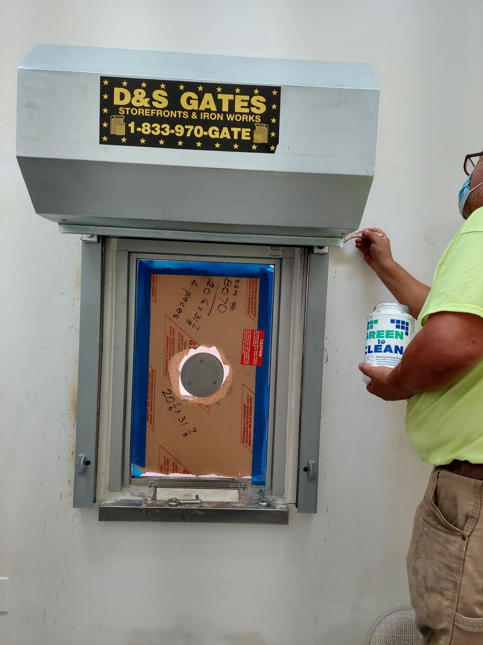 Worker painting a blue-framed service window beneath a D&S Gates sign.