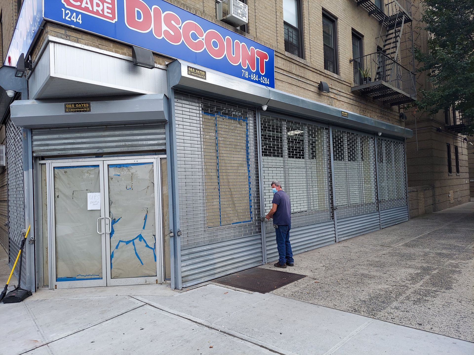 Corner storefront with a blue “DISCOUNT” sign, metal security grates, and a person standing by the entrance