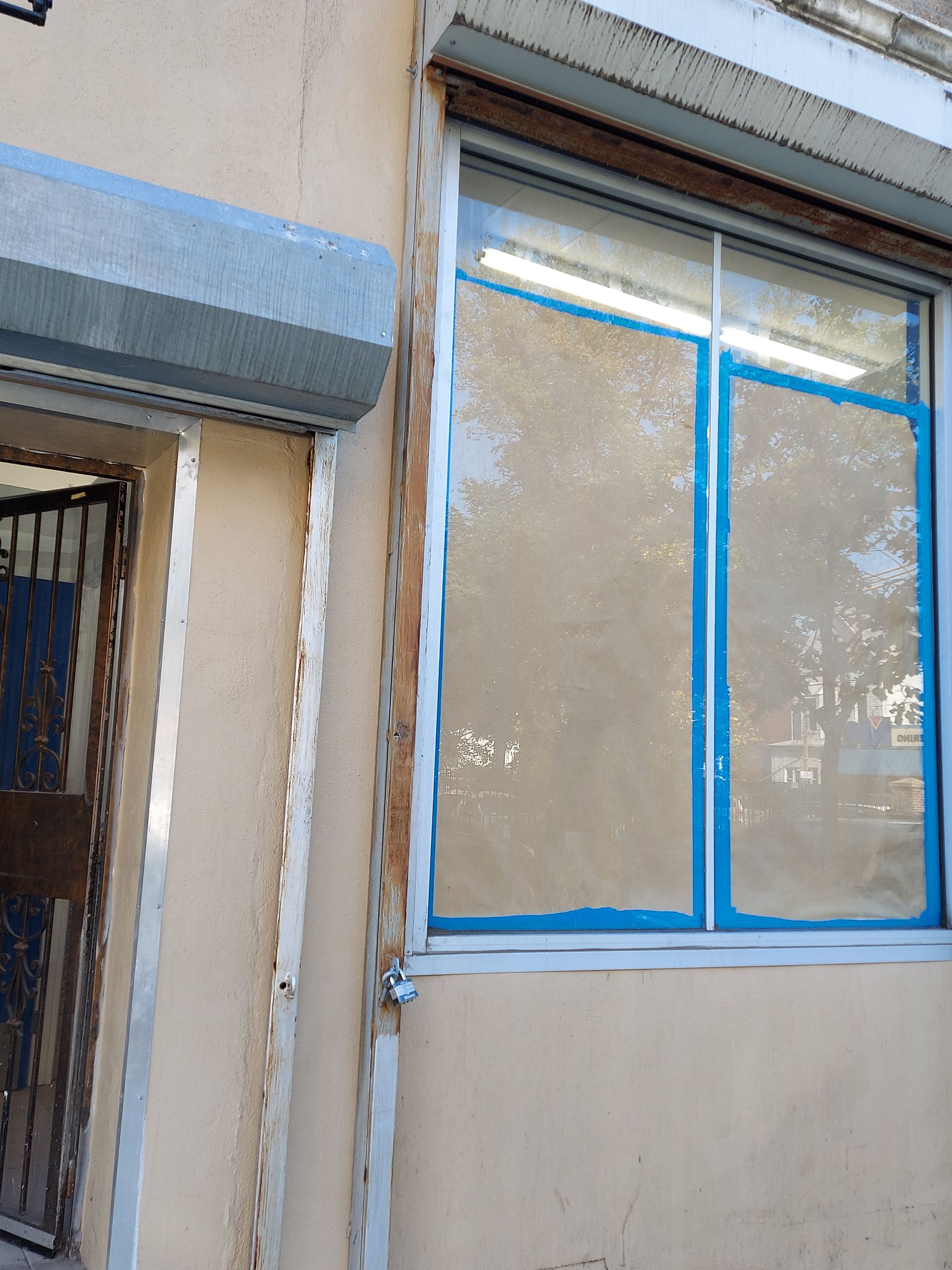 Exterior wall with a blue-trimmed window, taped edges, and a doorway on the left