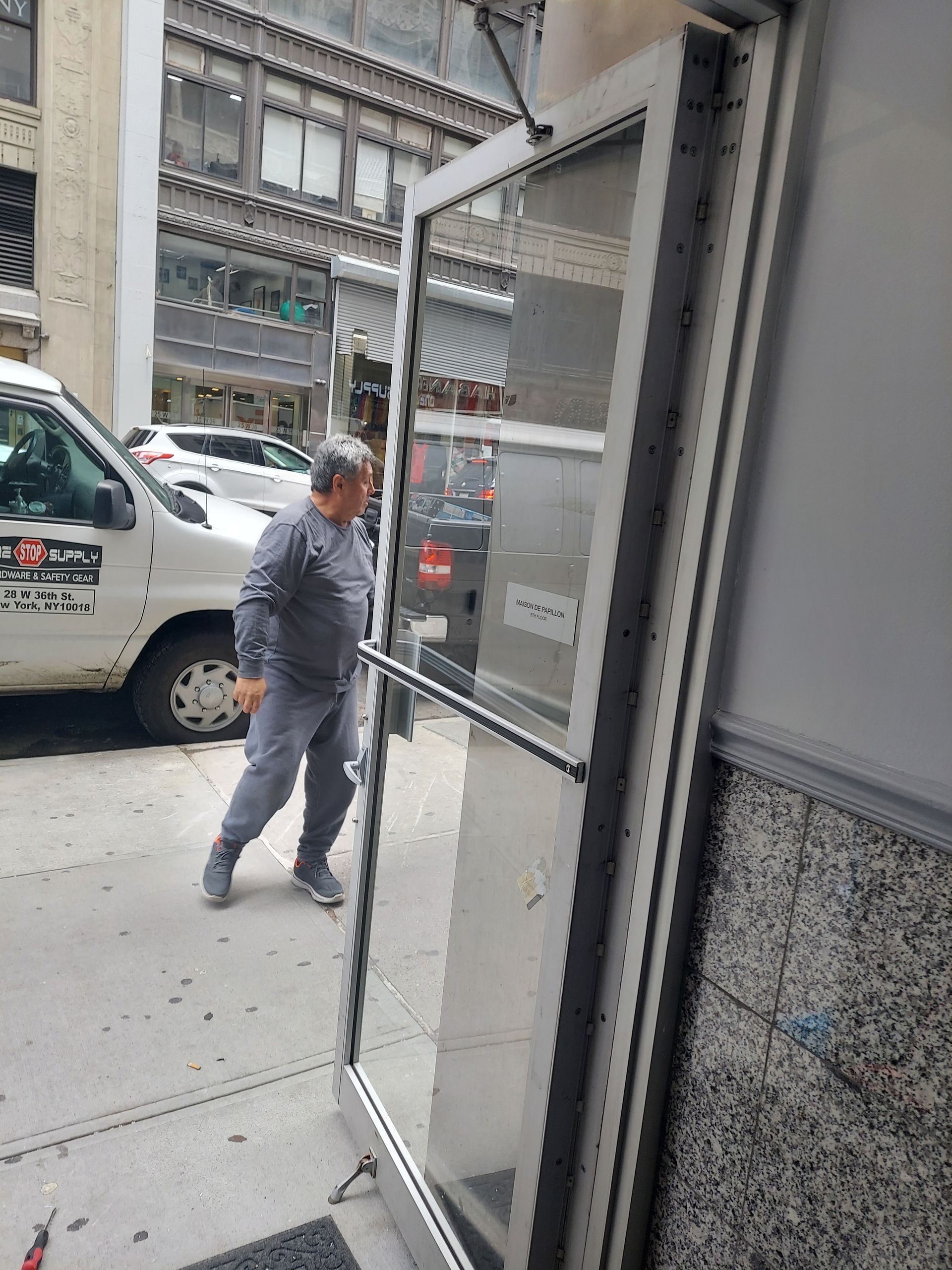 Man in gray work clothes entering a building through an open glass door on a city street.