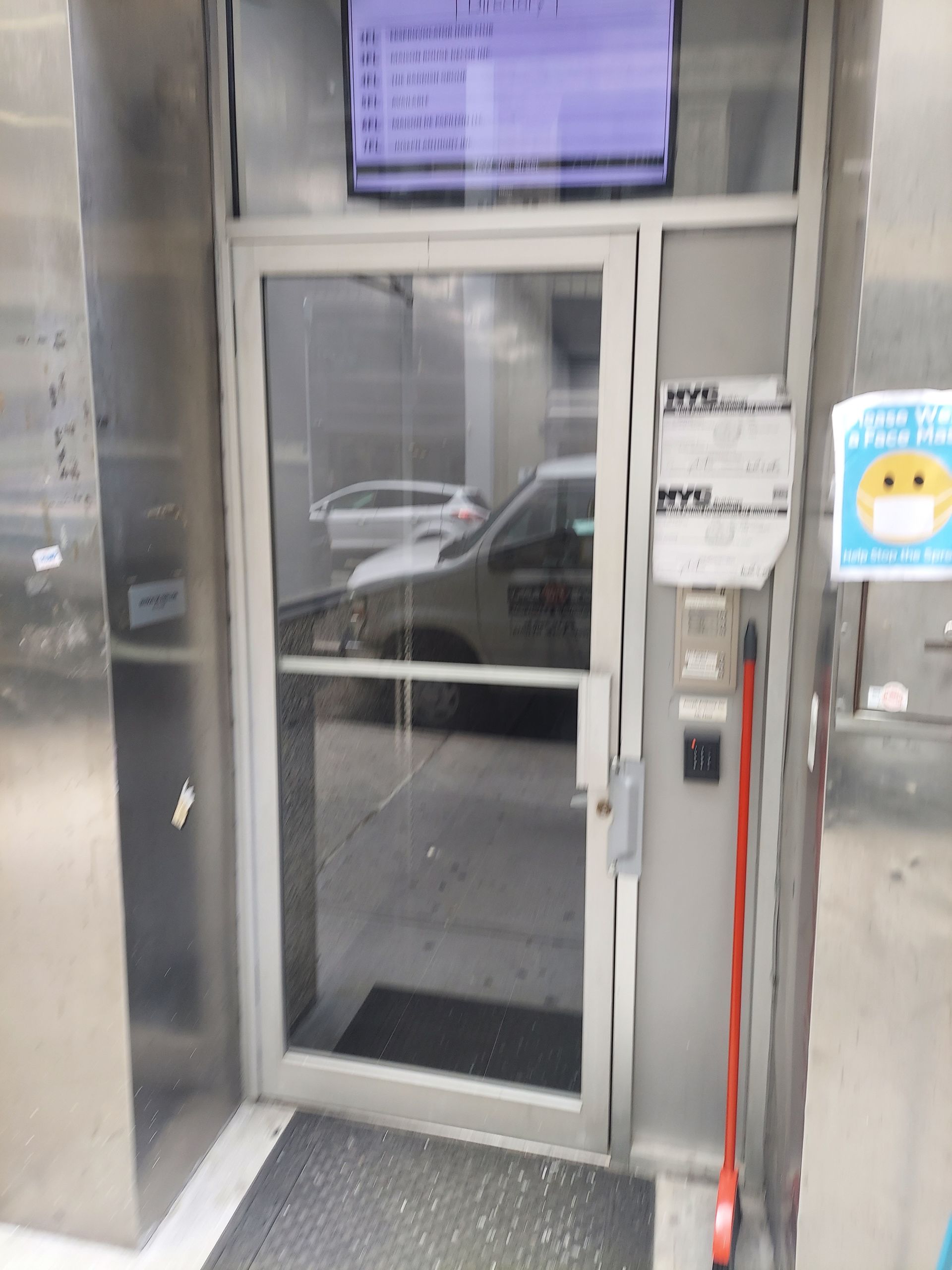 Glass storefront door with keypad and posted notices beside it