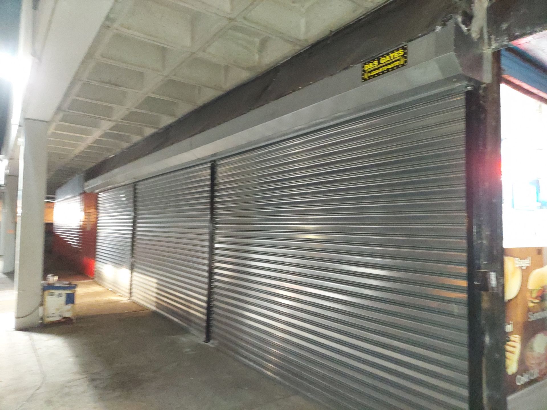 Closed silver metal security shutters at a covered walkway or storefront corridor