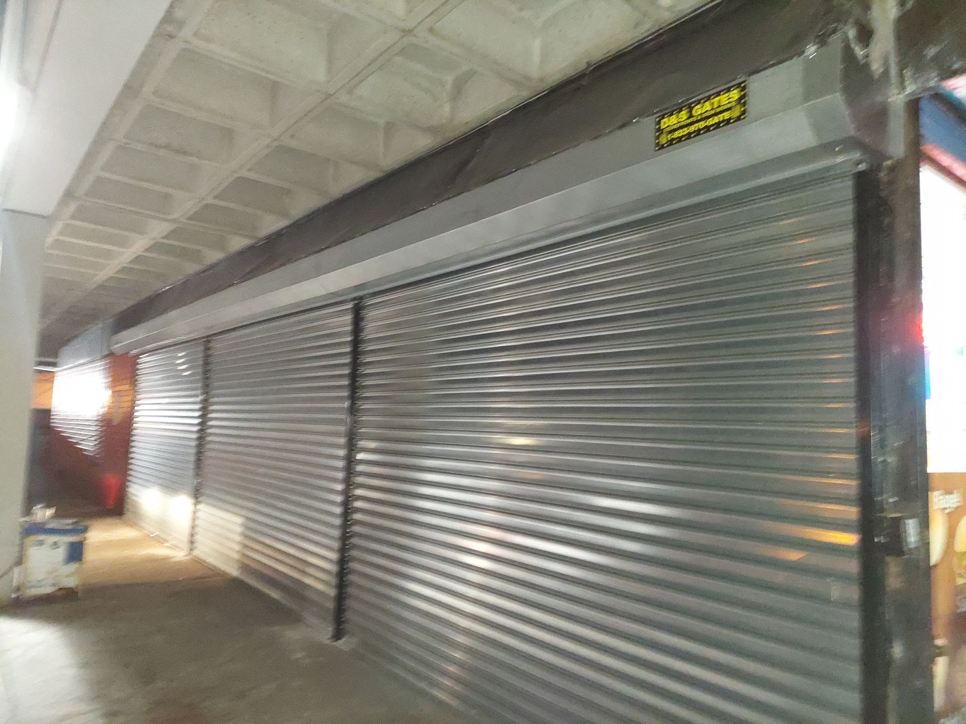 Closed metal storefront shutters in a covered walkway at night
