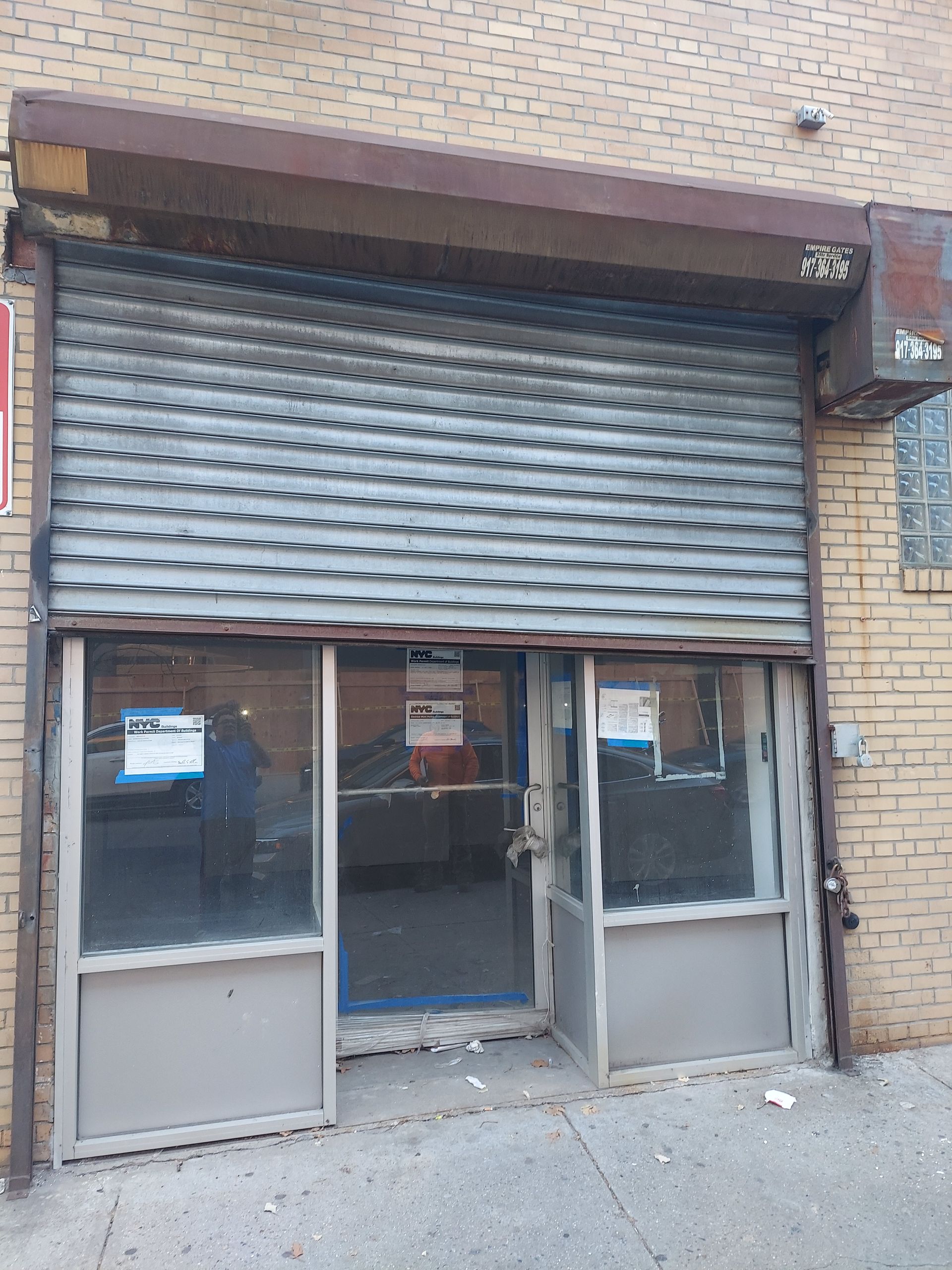 Closed storefront with metal roll-down shutter and glass double doors on a brick building