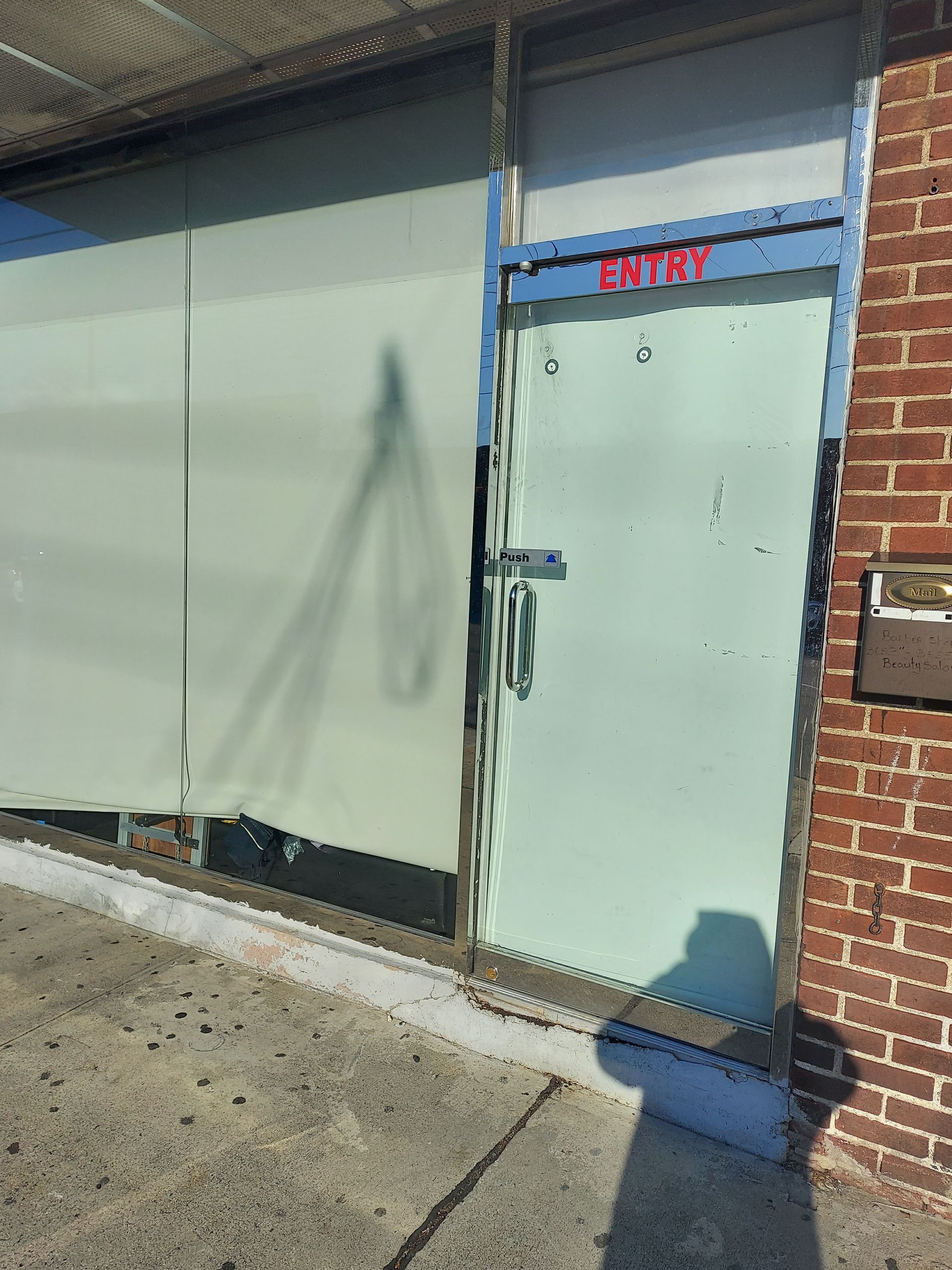Storefront entrance with a light blue door and gray window panels beside a brick wall.