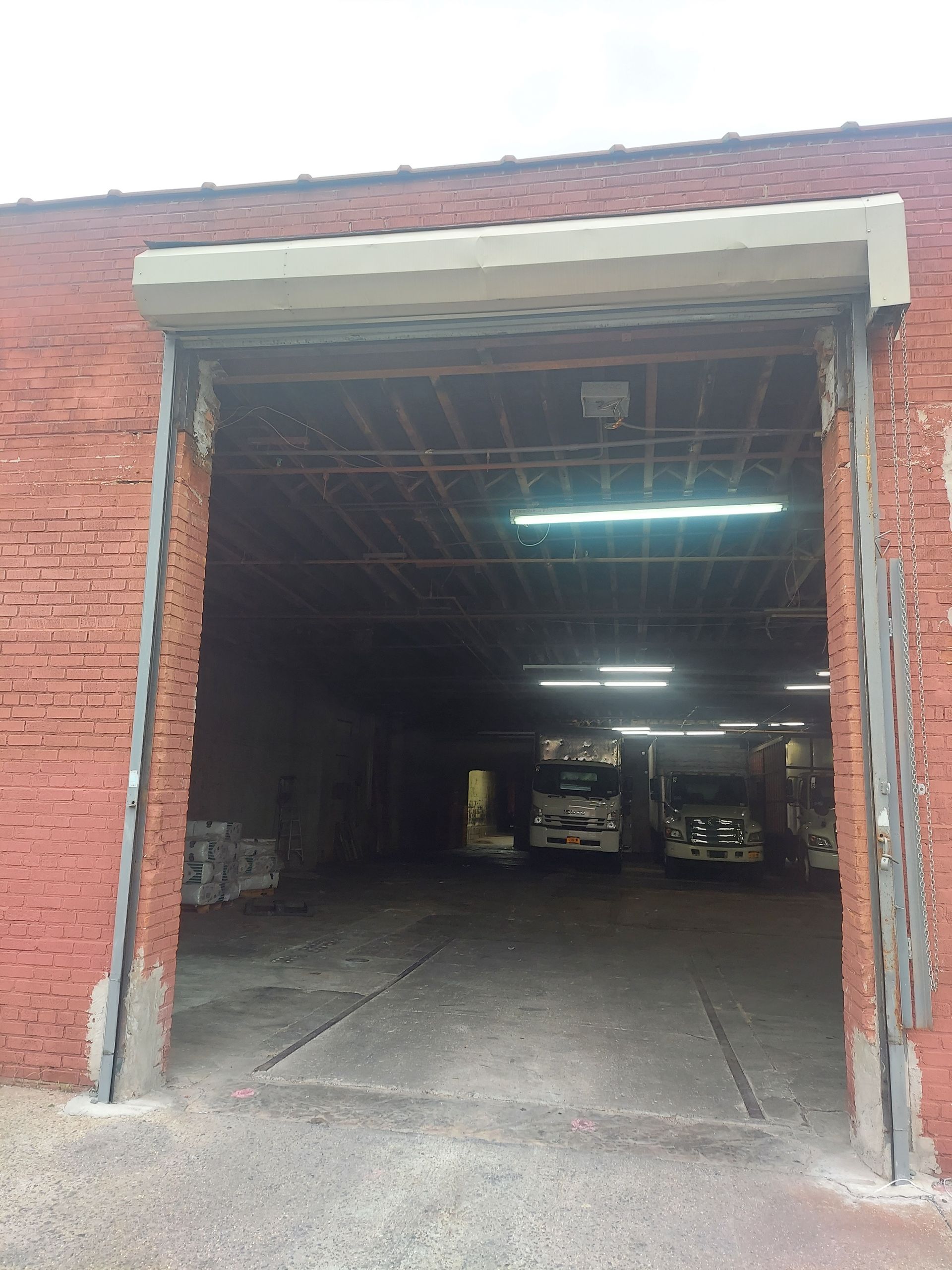 Open industrial garage with red brick walls, concrete floor, and fluorescent lights inside