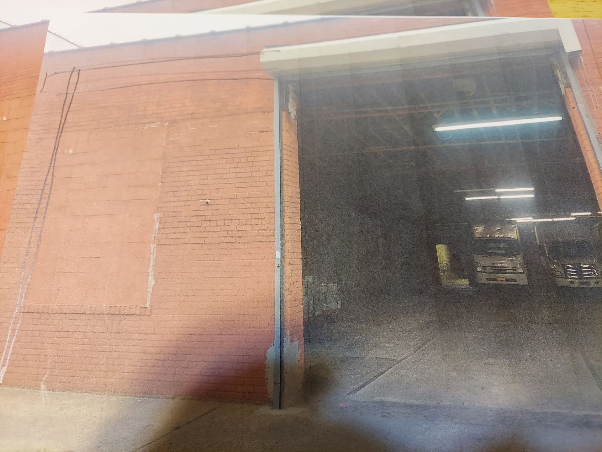 Exterior of a brick building with a large open garage-style doorway and bright overhead lights inside.