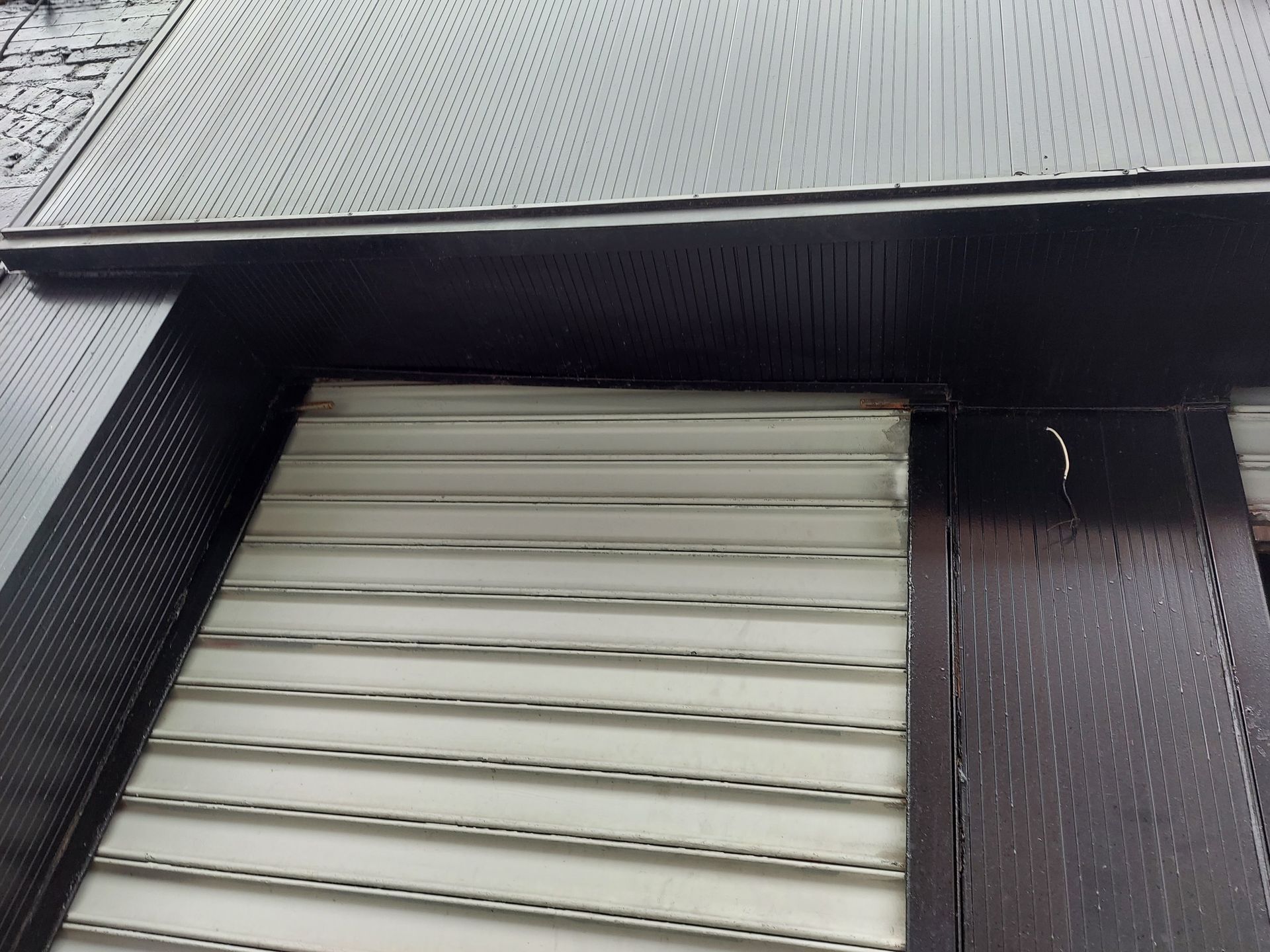 Exterior of a building with a closed white roll-up shutter under dark metal siding