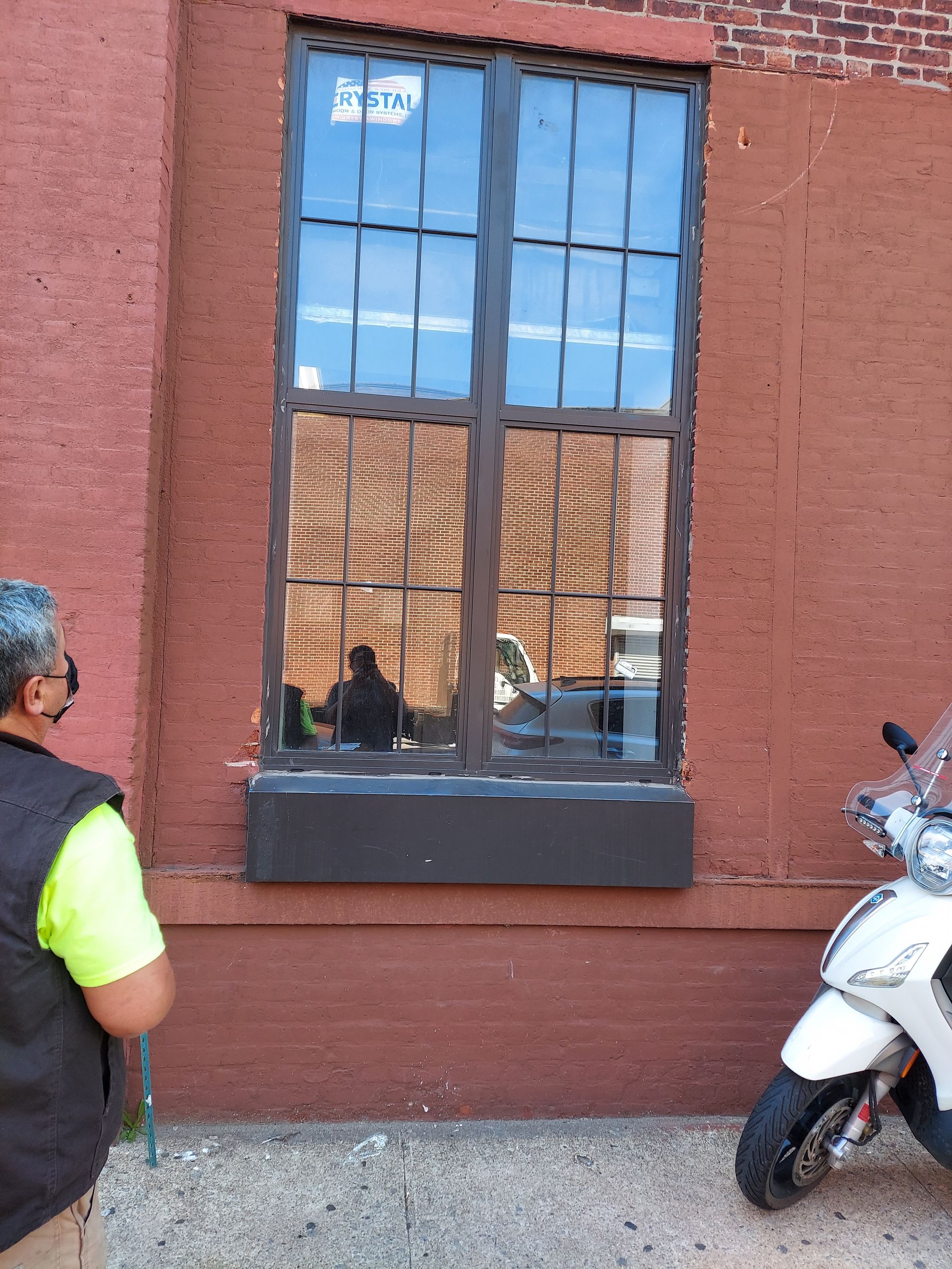 Red brick building with a reflective window and a white scooter parked beside it.