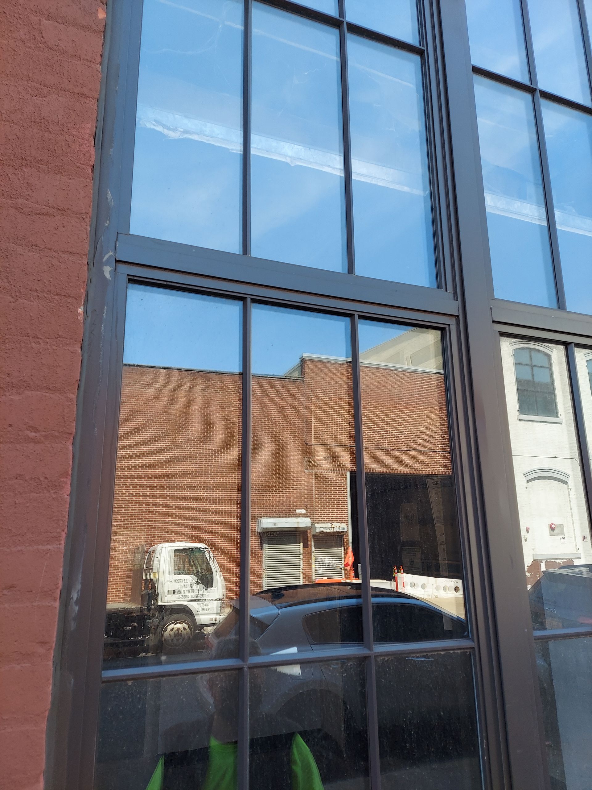 Modern glass storefront reflecting parked vehicles and brick buildings
