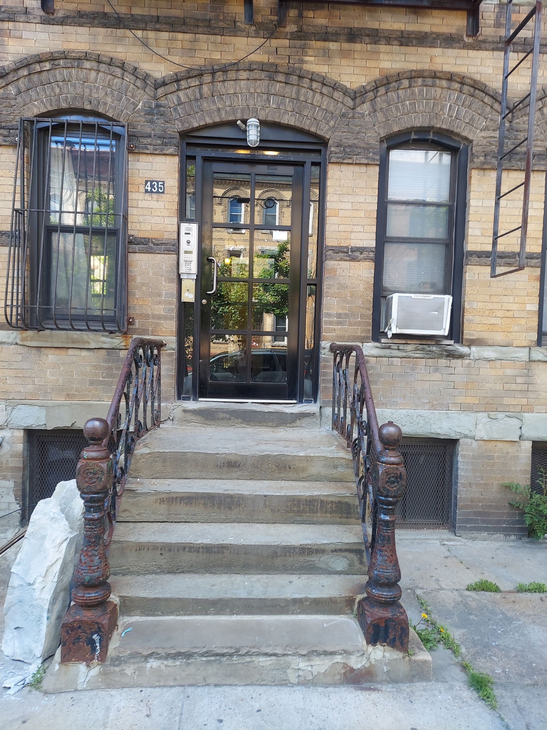 Brick apartment stoop with central concrete steps, black metal railings, and a glass entry door.