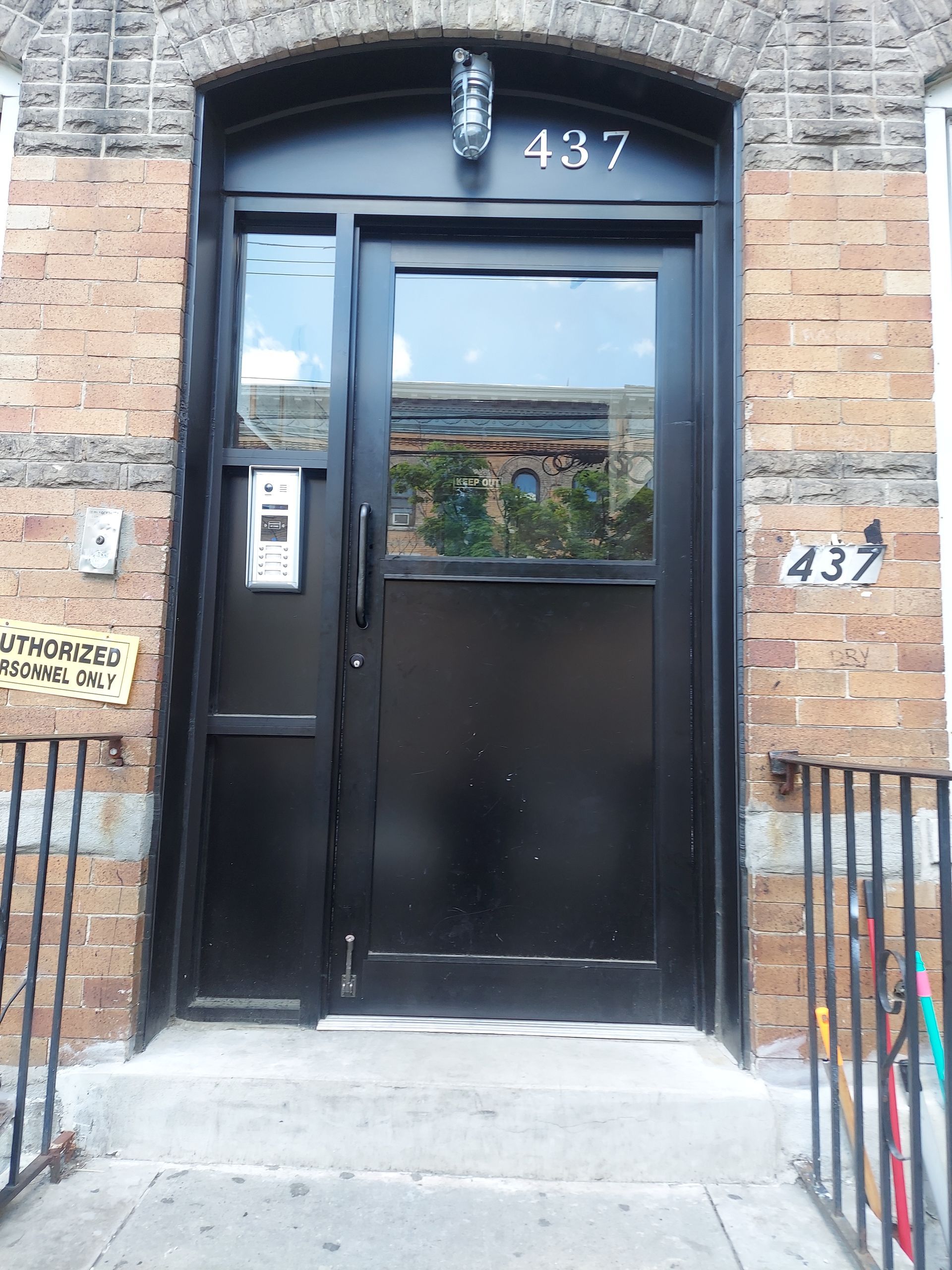 Black door entrance at 437 with intercom, stone facade, and metal railing on a city sidewalk.