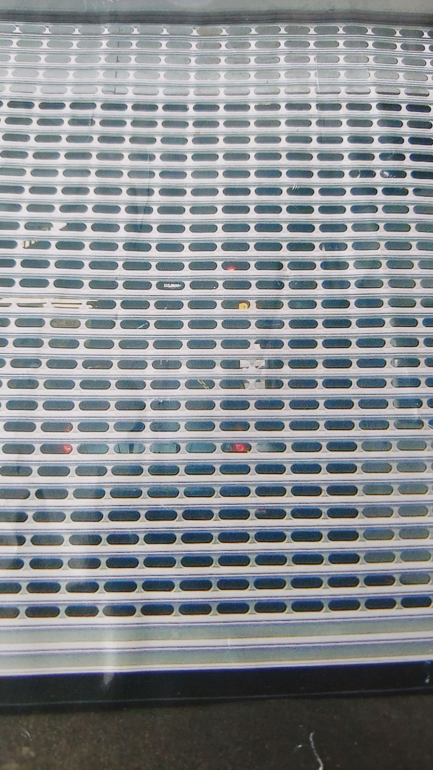 Metal mesh grille with rows of slats and a dark surface behind it