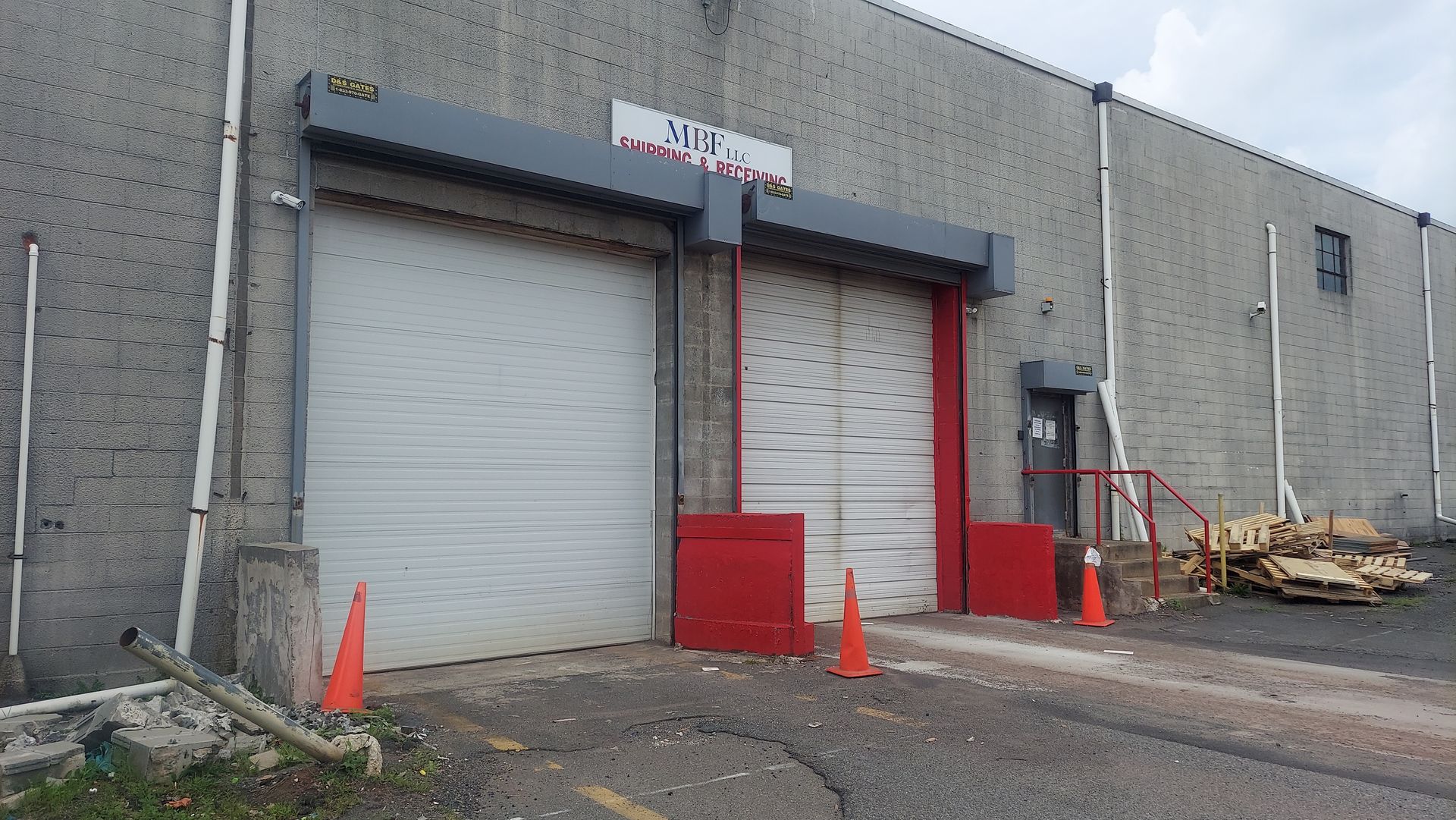 Industrial warehouse loading docks with two closed roll-up doors, orange cones, and stacked pallets