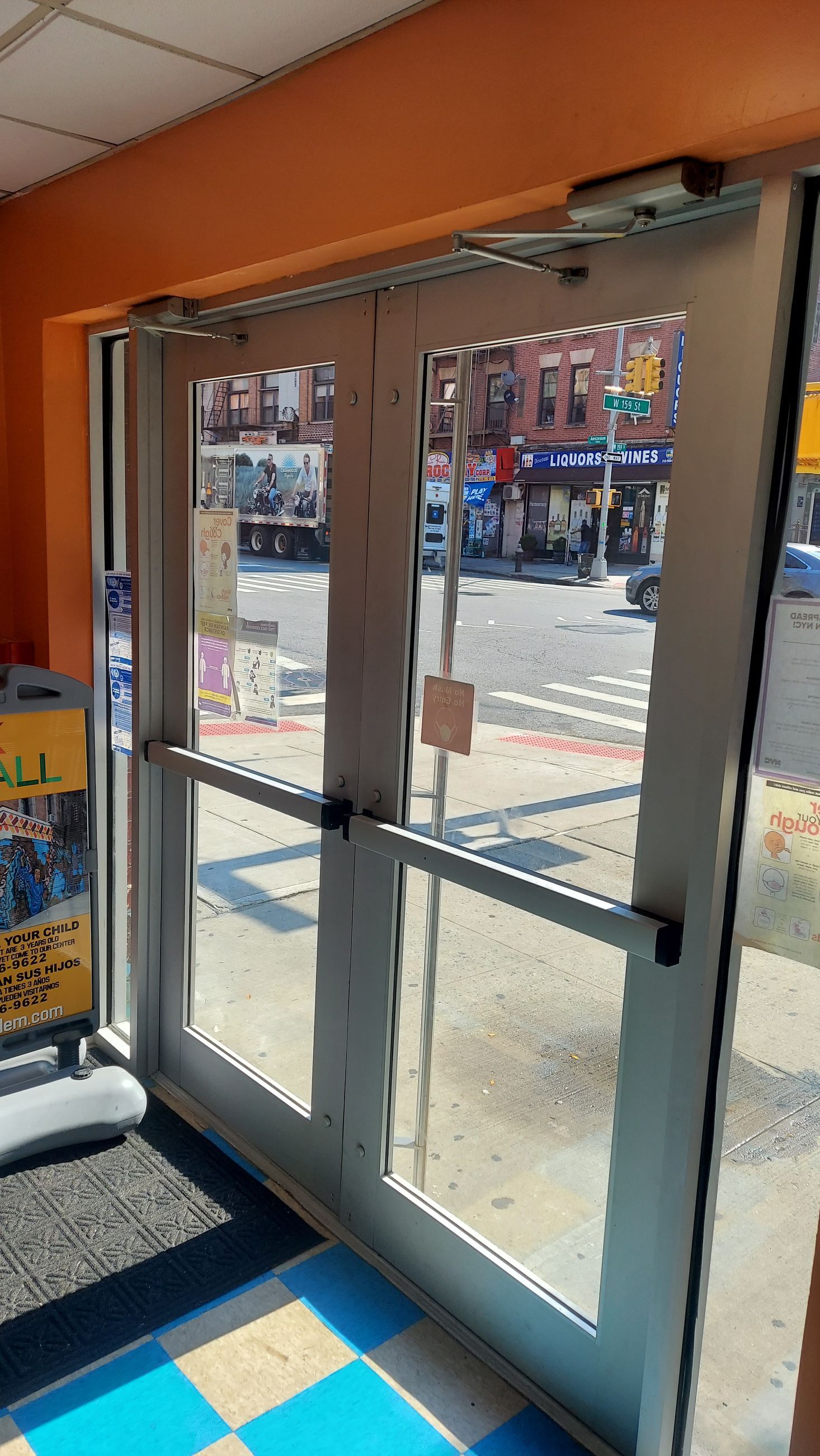 Glass storefront doors opening to a busy street outside, with orange awning and blue-tiled floor inside.