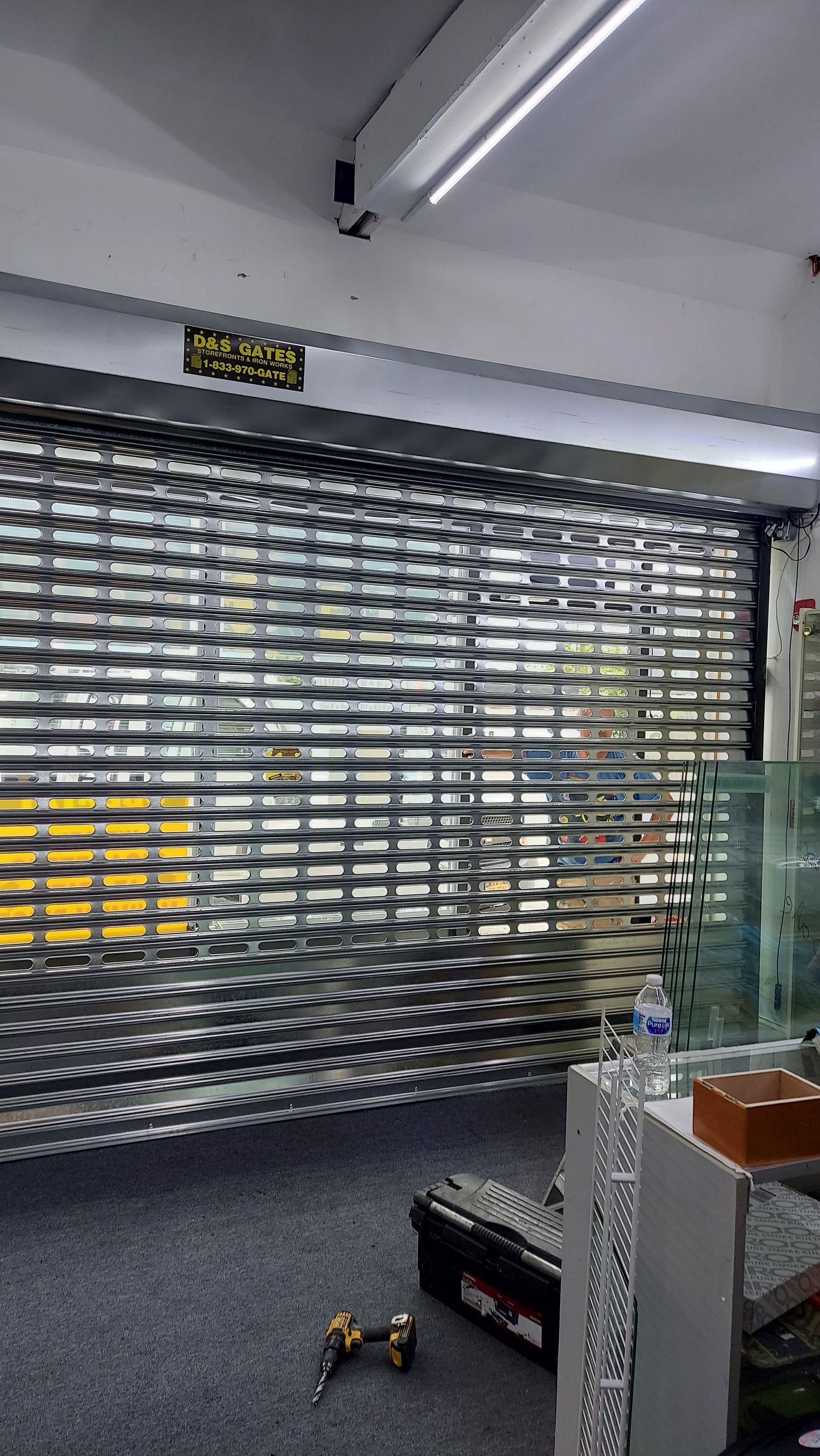 Closed metal security gate inside a store, with tools and a counter in the foreground.
