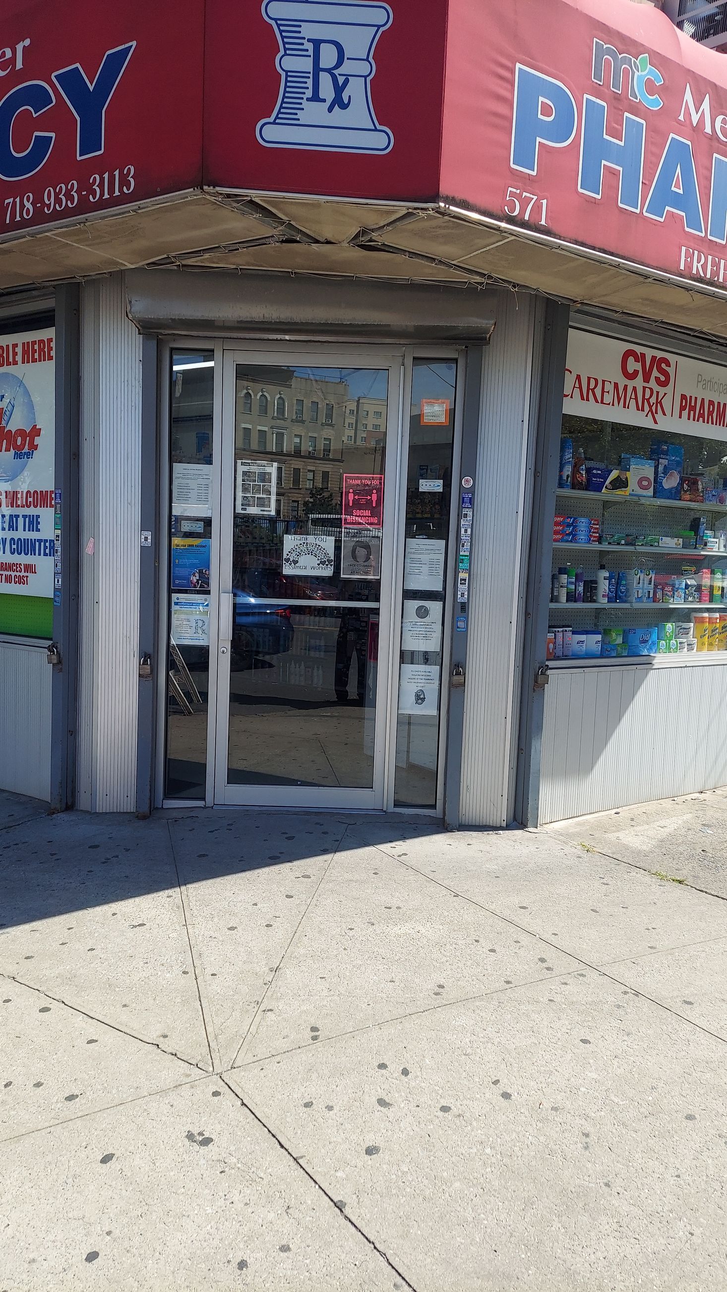 Corner storefront pharmacy with red awning and glass entrance, viewed from the sidewalk