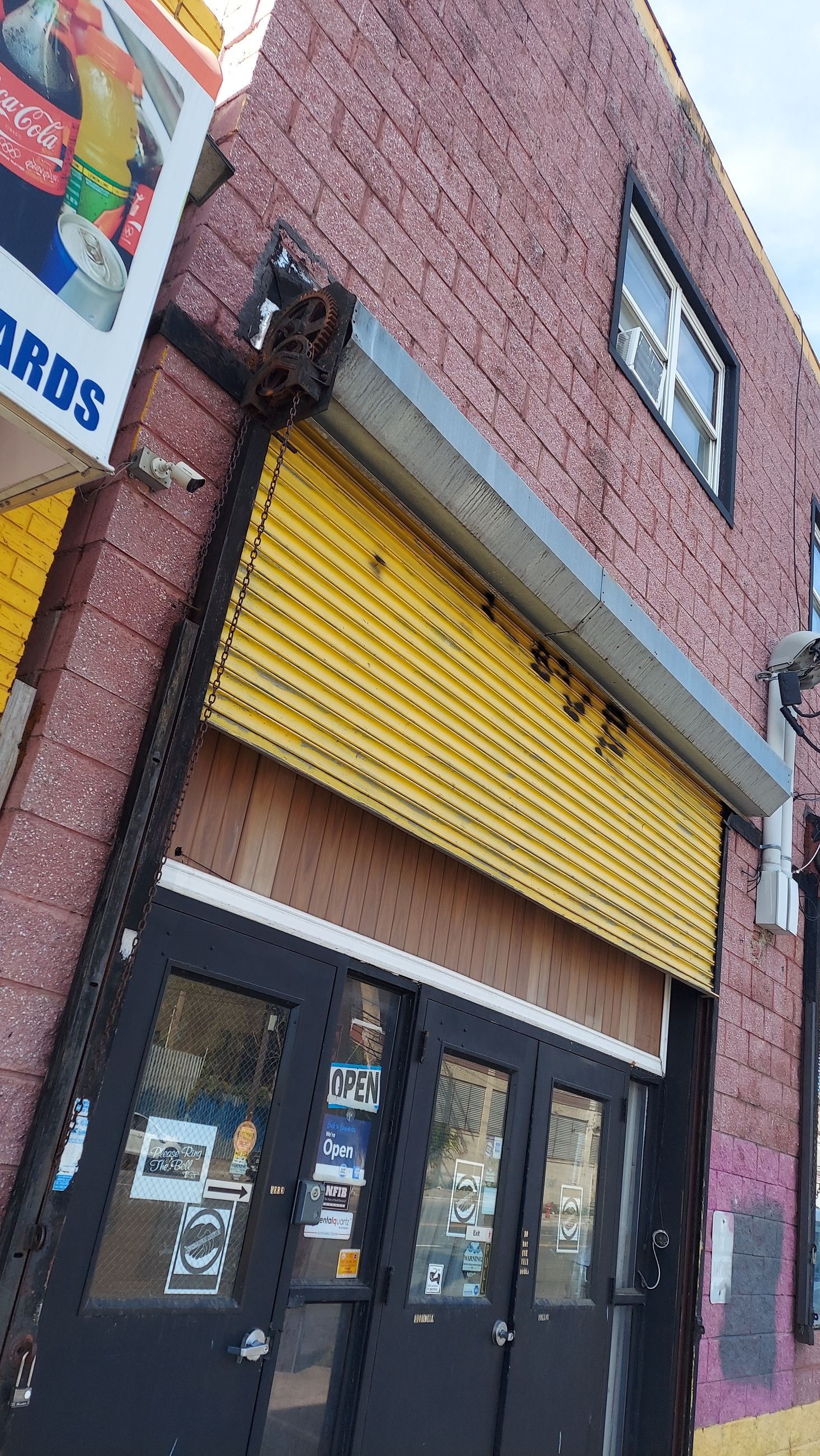 Brick storefront with yellow awning and black double doors on a narrow street