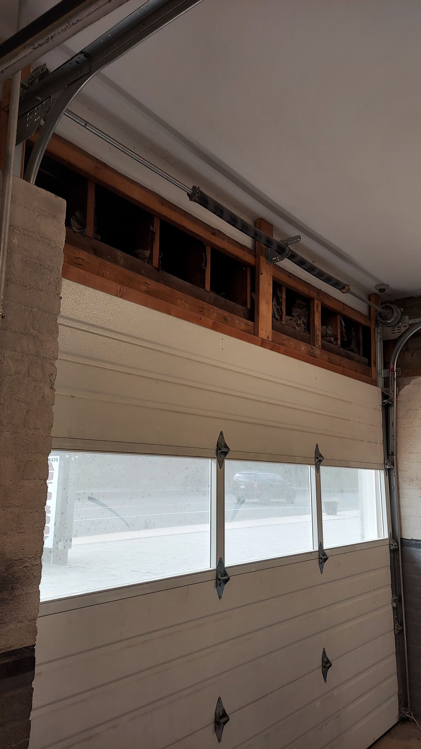 Closed white garage door with small windows inside a garage, showing exposed wood framing above.