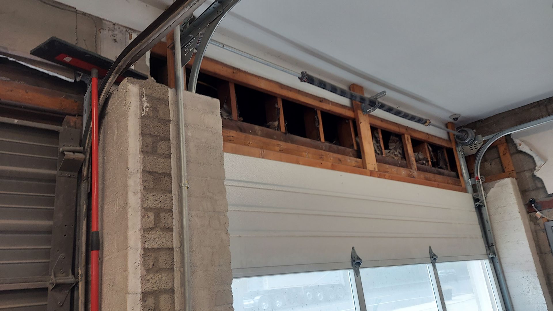 Partially demolished garage door opening with exposed framing and drywall above a window