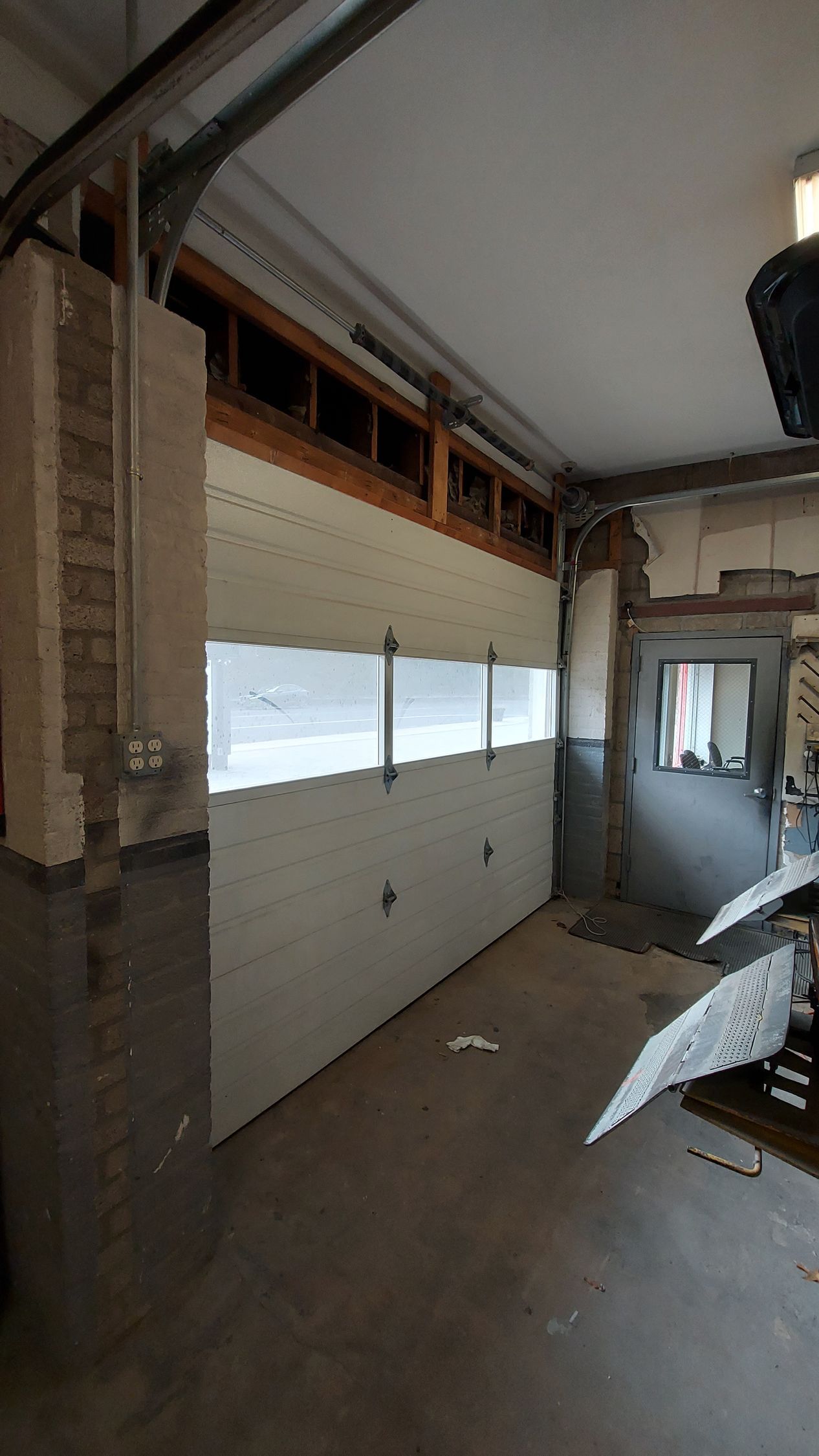 Interior of a garage under renovation, with a white sectional door and exposed framing.