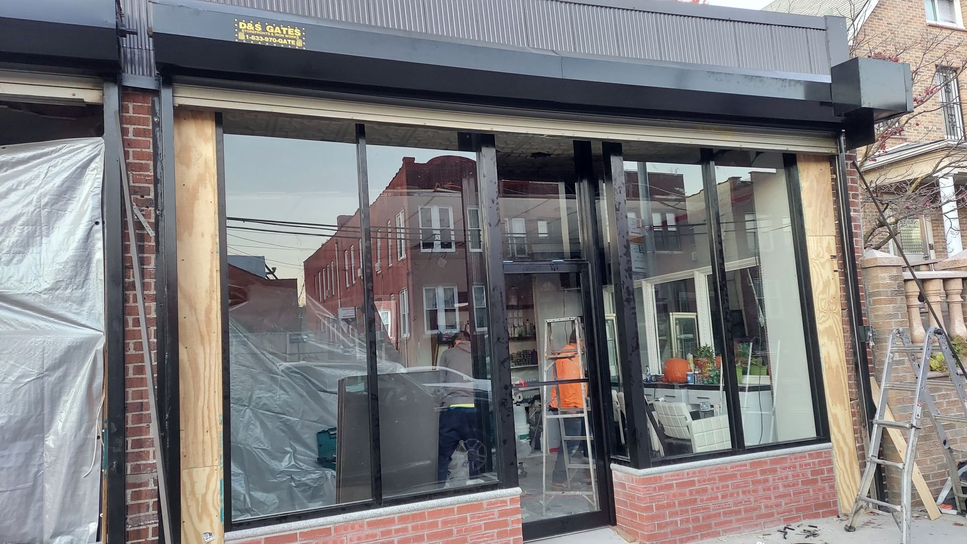 Storefront with large glass windows, black awning, and brick base on a city street.