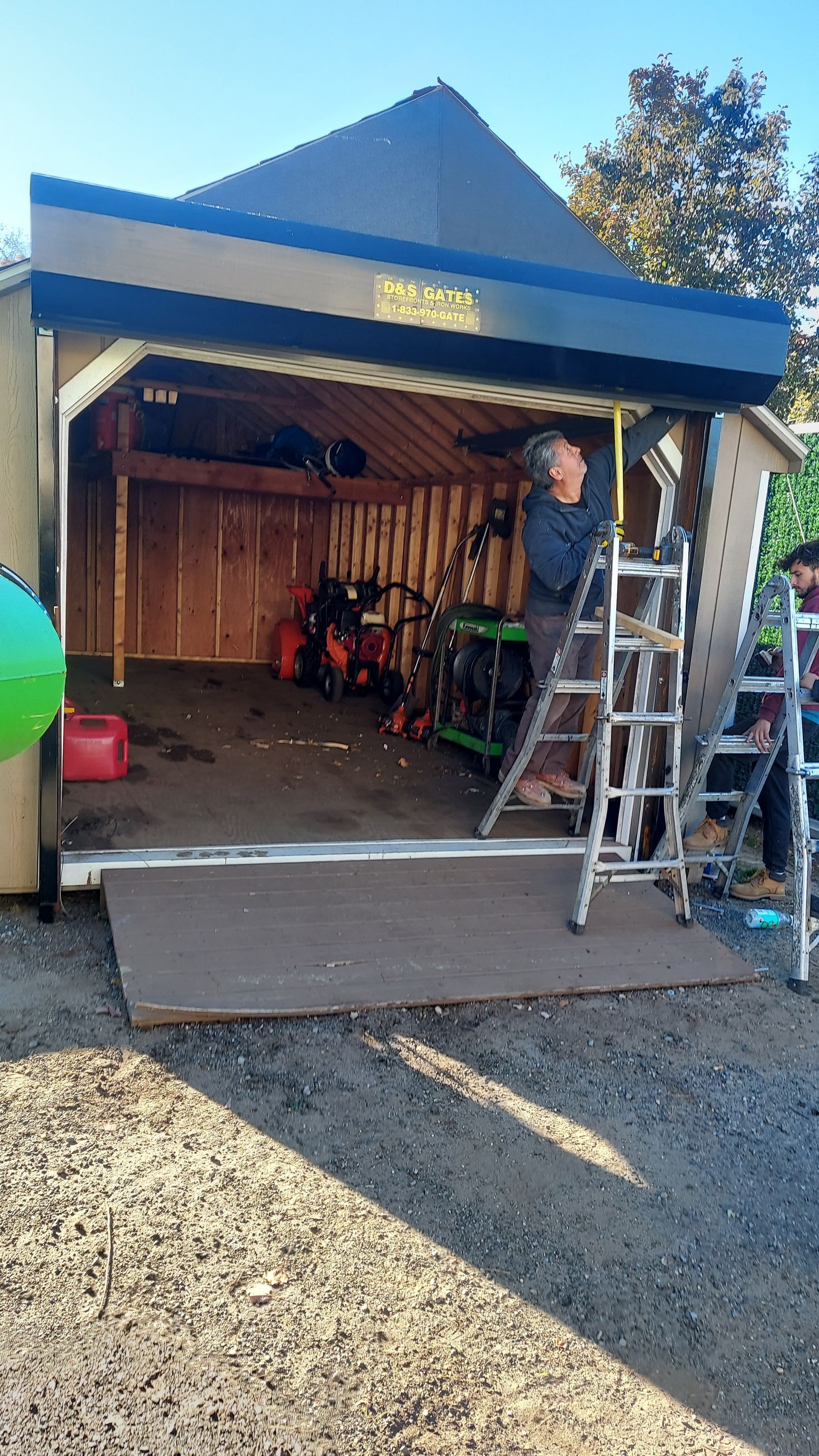 Open garage/workshop with a ramp, ladder, tools, and a person inside, in daylight