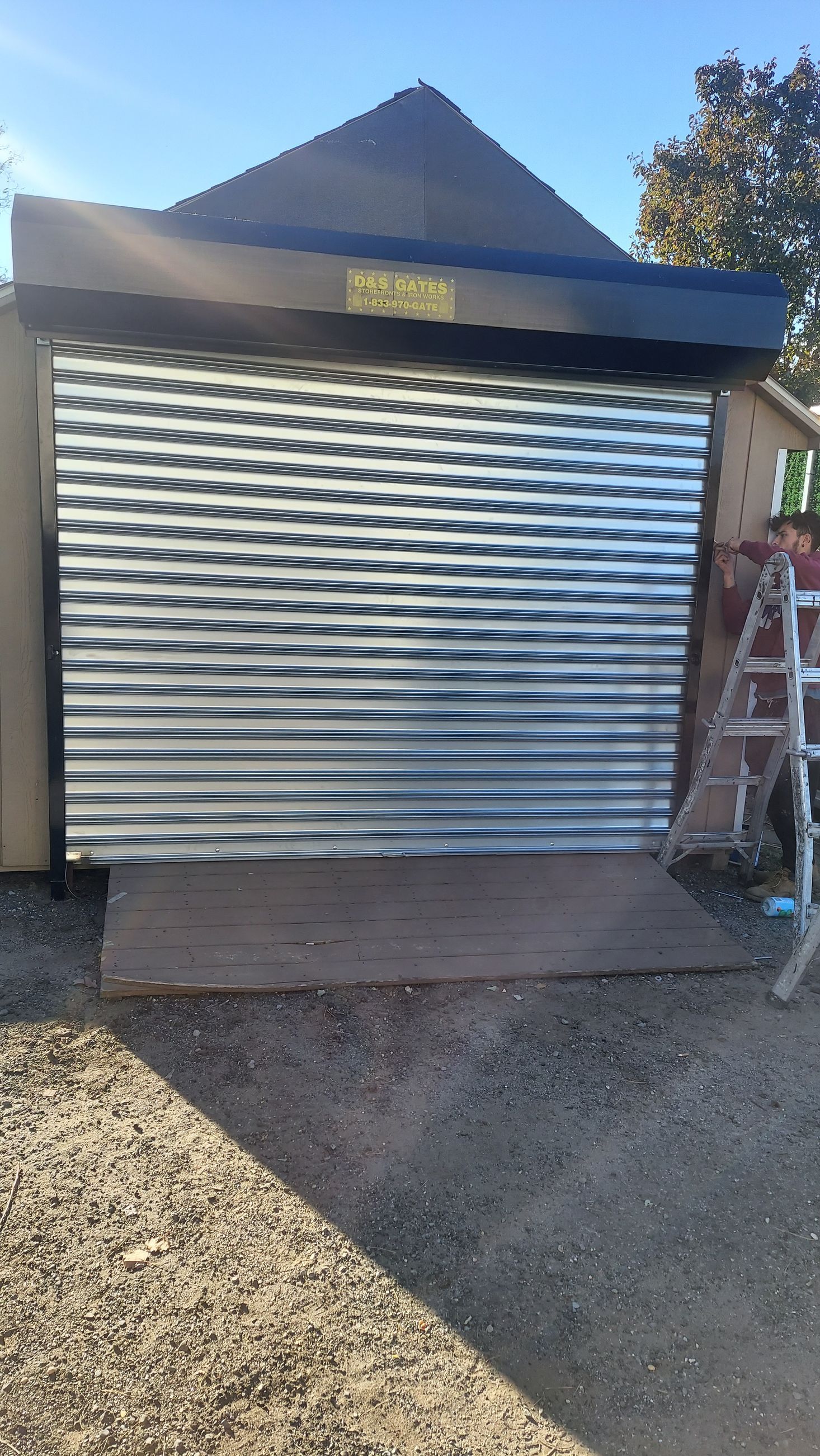 Closed metal roll-up garage door with a wavy reflection, set in a small outdoor driveway area.