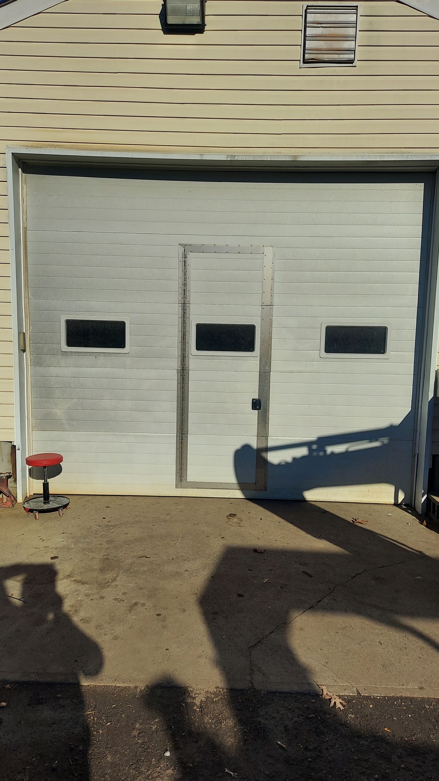Closed white garage door with three small windows on a beige building, in bright sunlight.