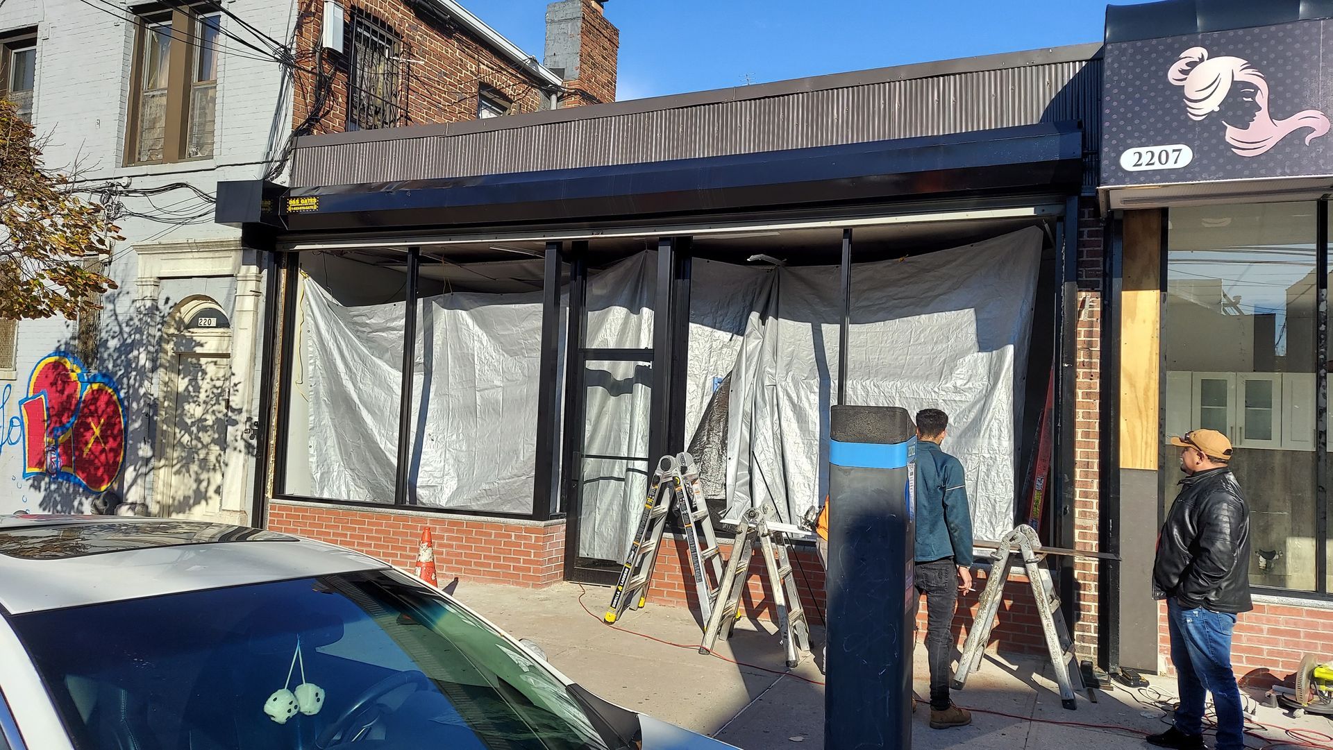Storefront under renovation with ladders and two people standing outside on the sidewalk