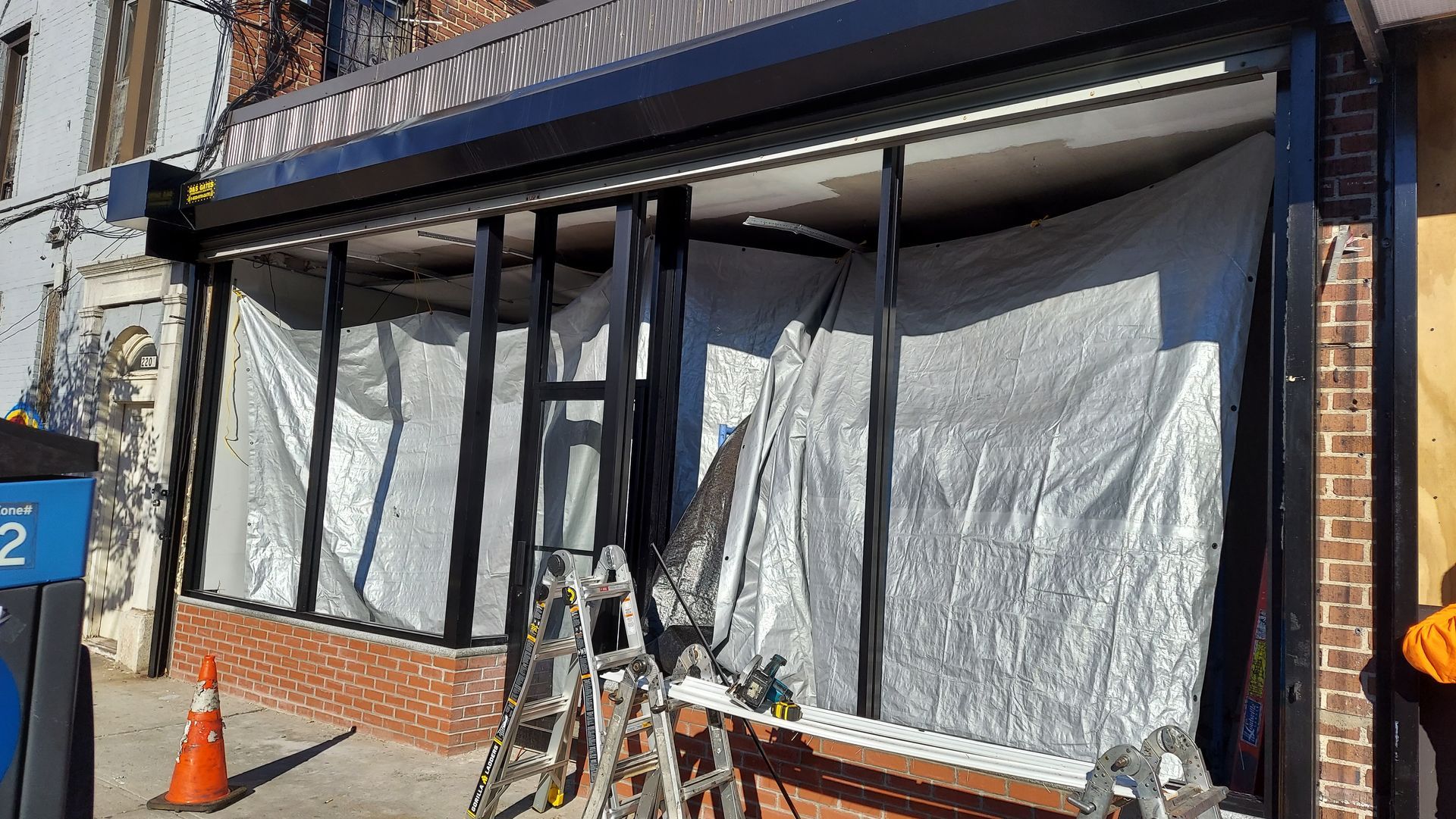 Storefront with black awning and white plastic sheeting covering a damaged or closed entrance, with orange cones in front