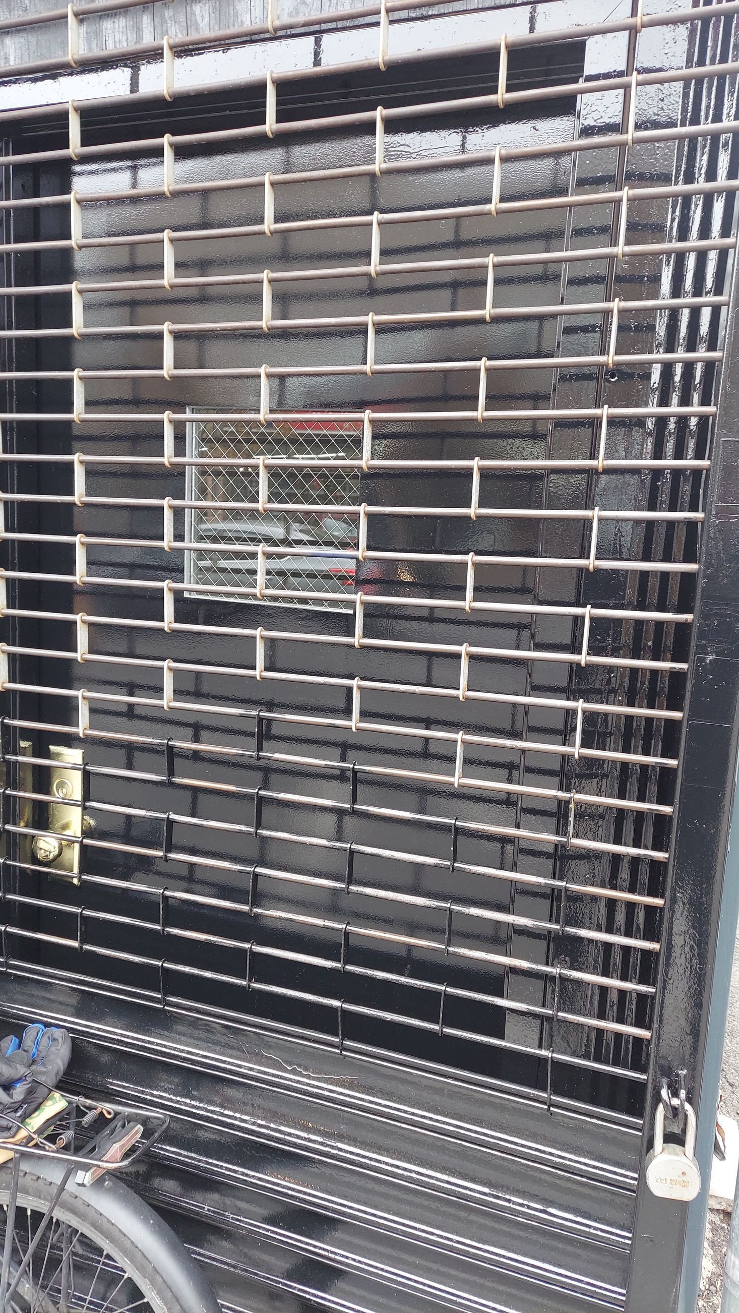 Black metal security gate with horizontal slats and a padlock on a storefront entrance