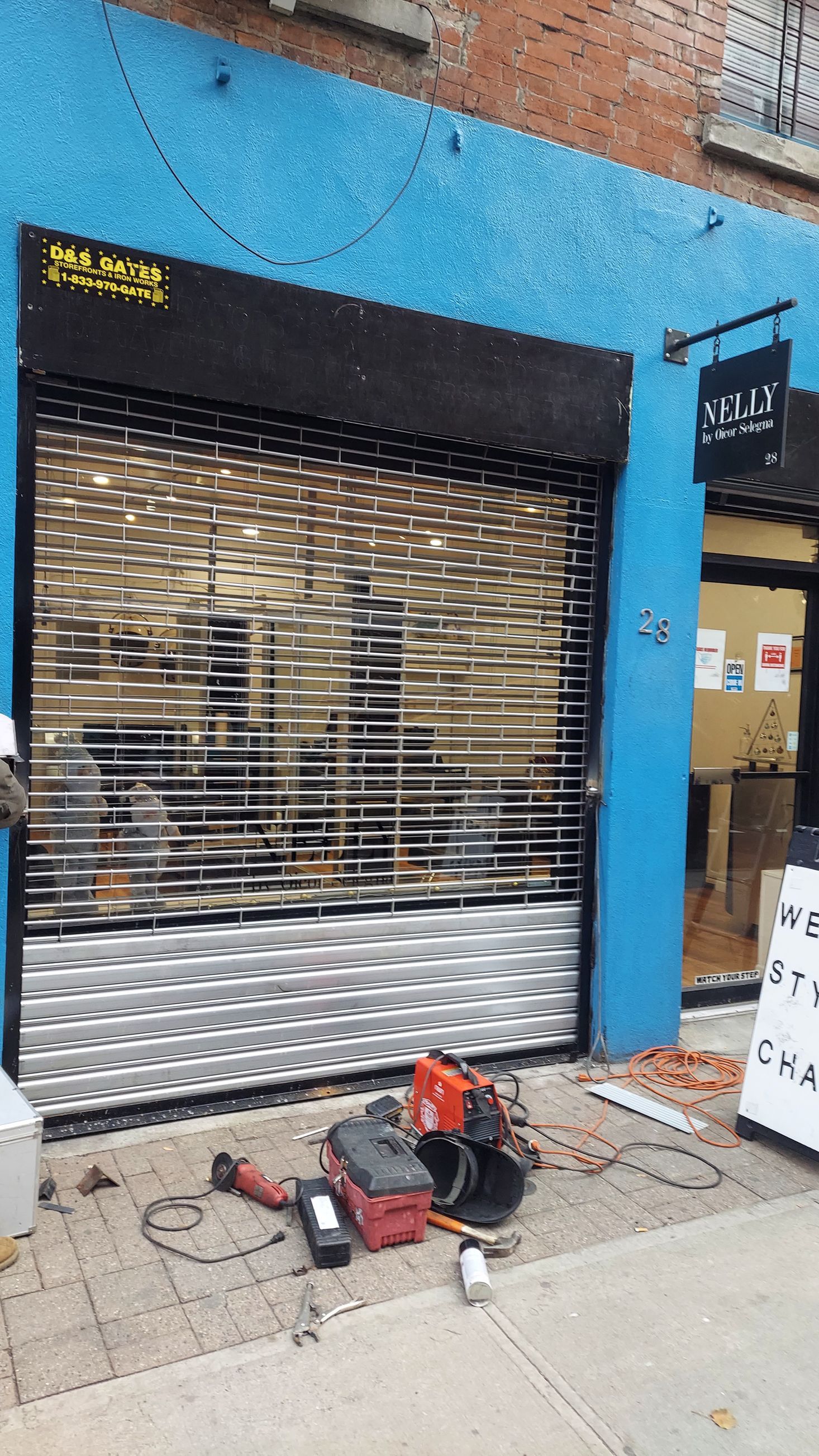 Blue storefront with closed metal shutter and tools on the sidewalk in front