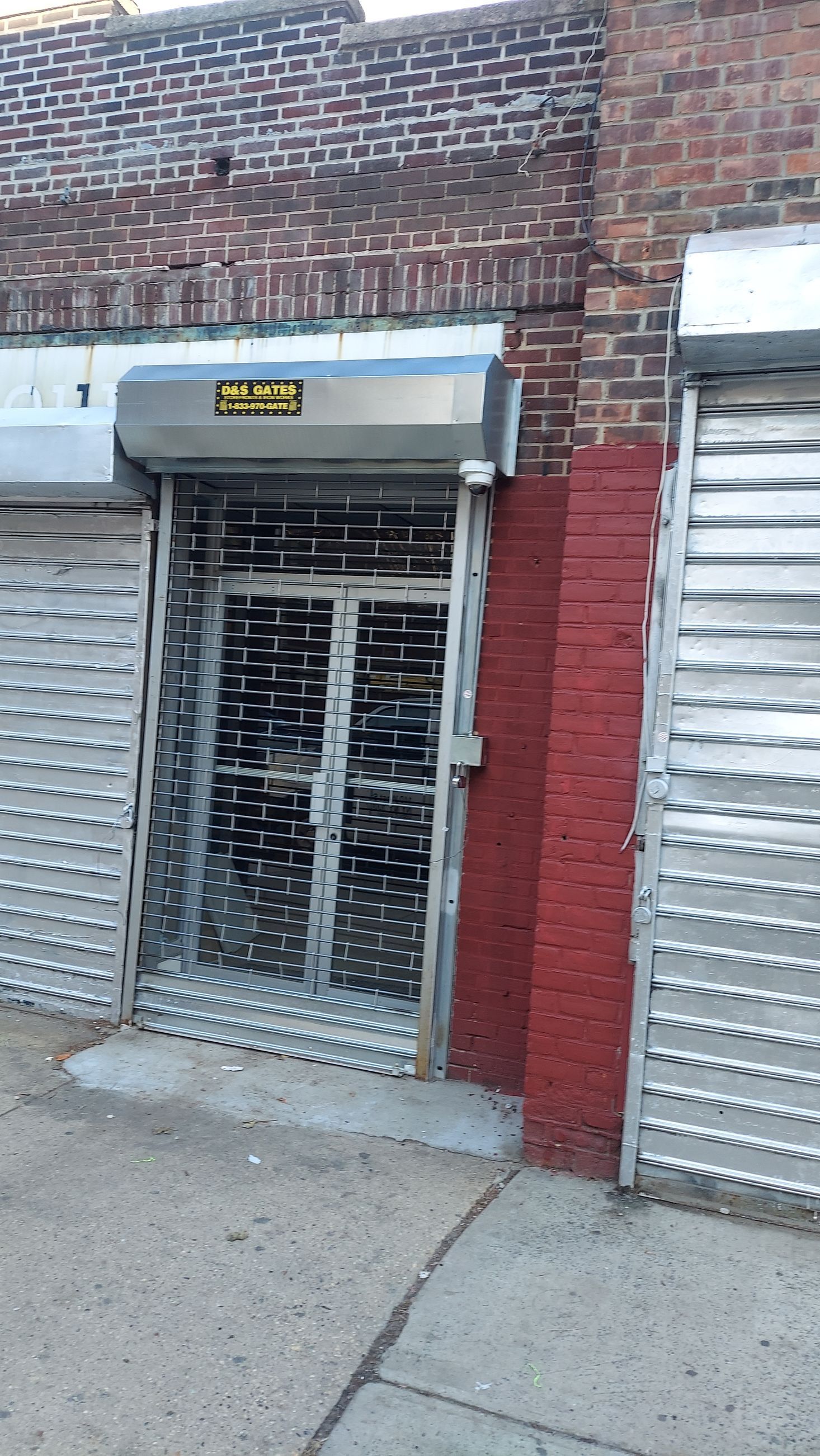 Closed storefront with metal security gates and a brick facade at a city sidewalk entrance
