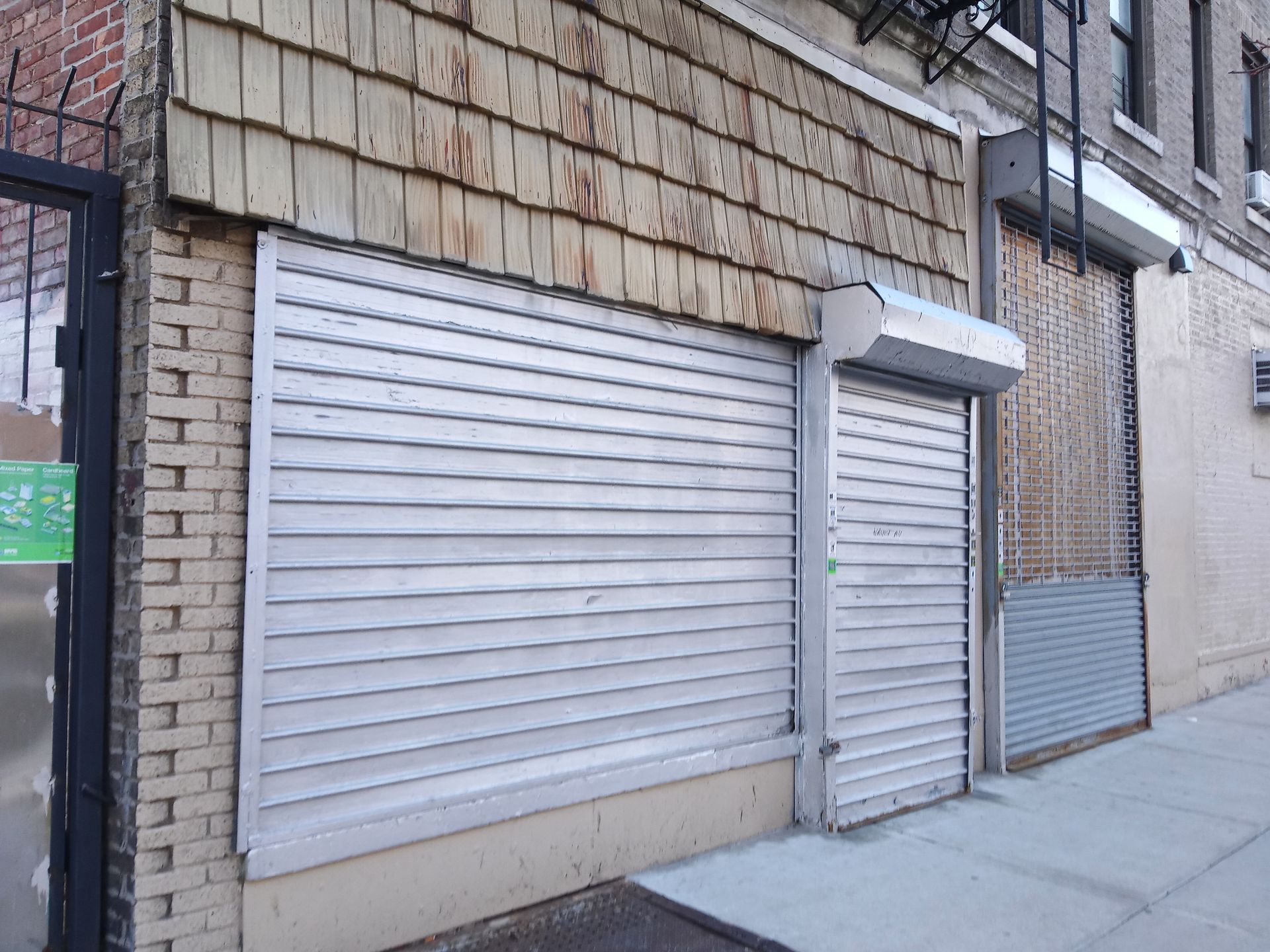 Closed storefront shutters on a sidewalk in front of a brick building