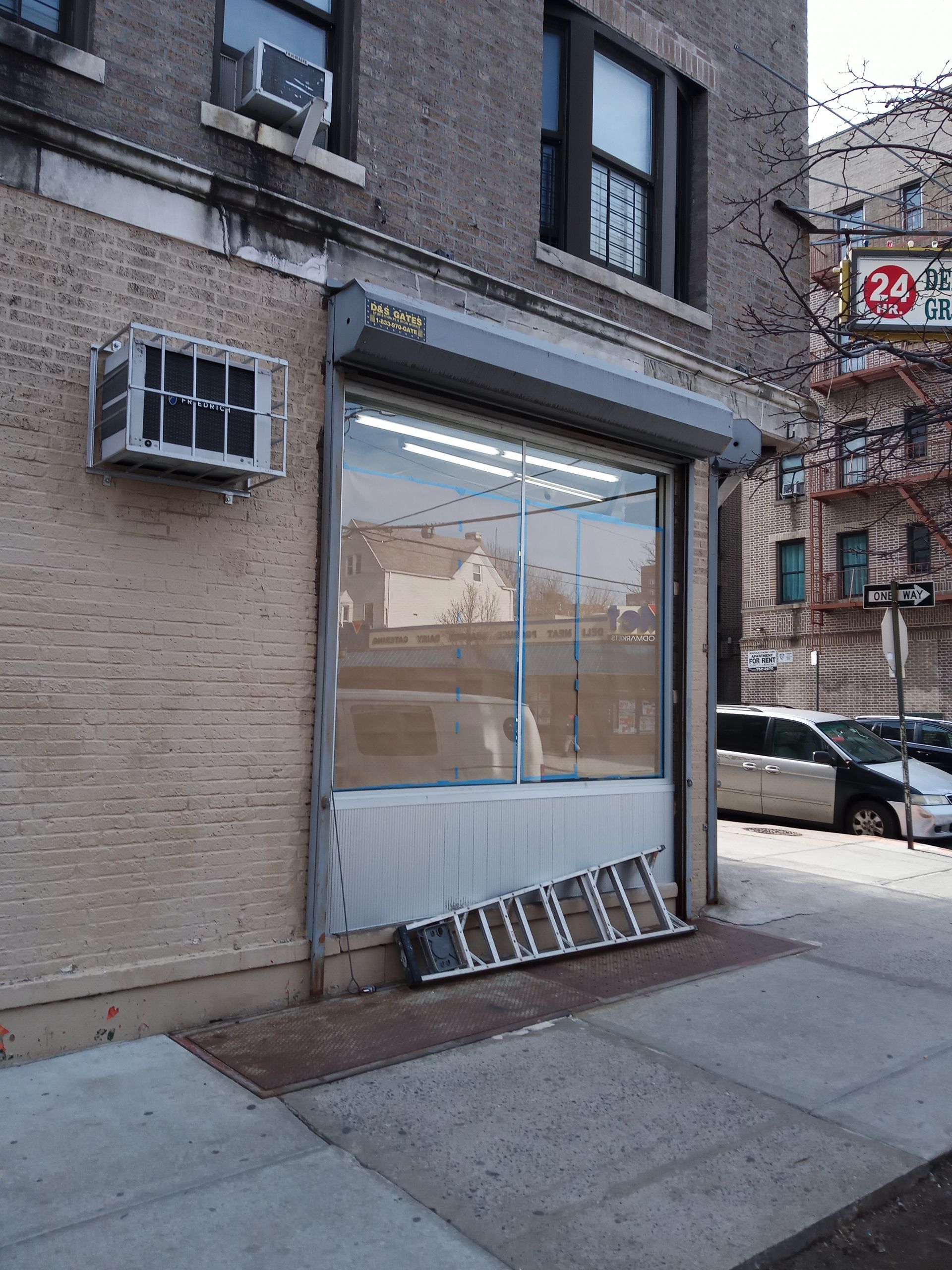 Storefront on a city sidewalk, with broken lower window panels and a parked car in the background.