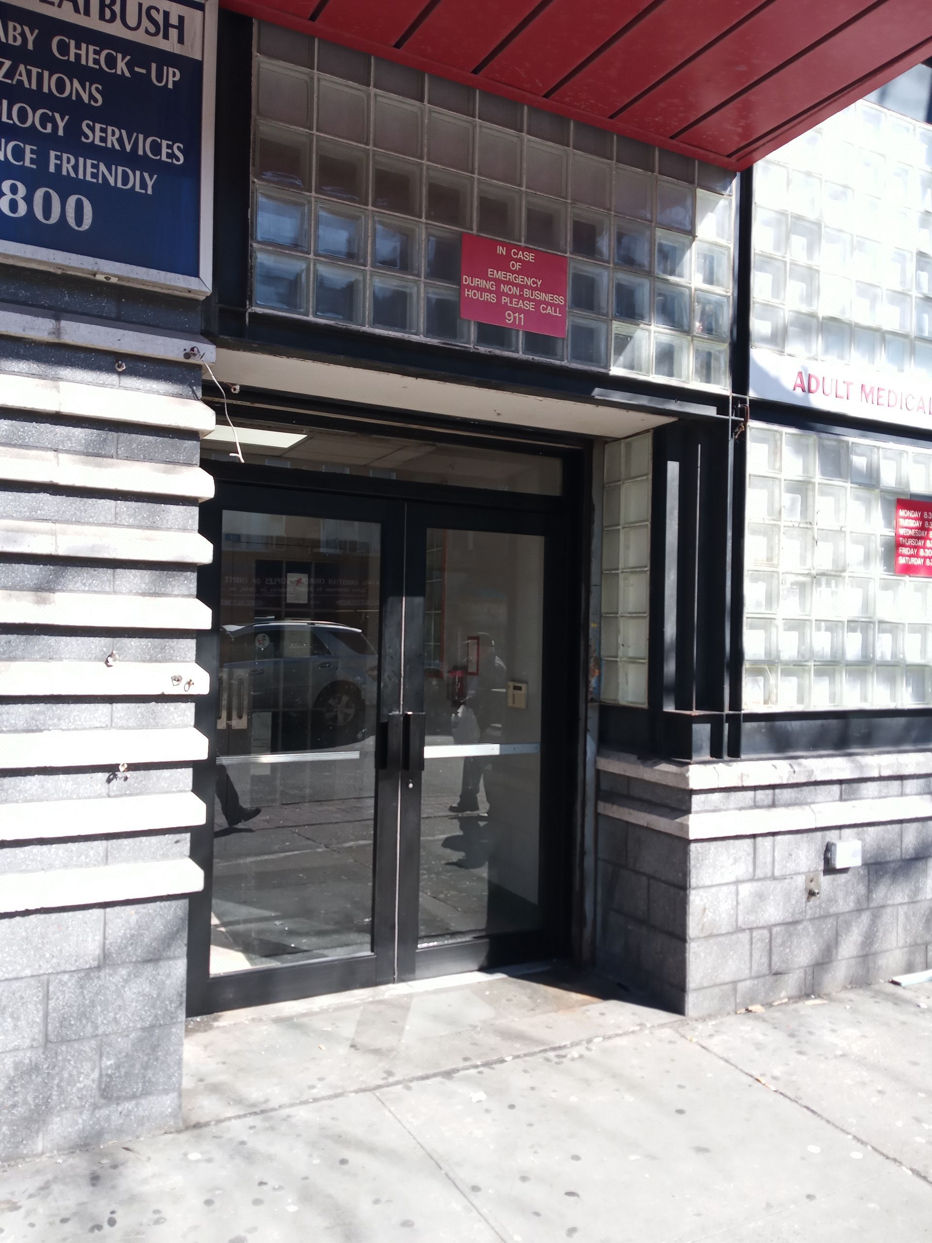 Storefront entrance with glass double doors and a red awning over a sidewalk.