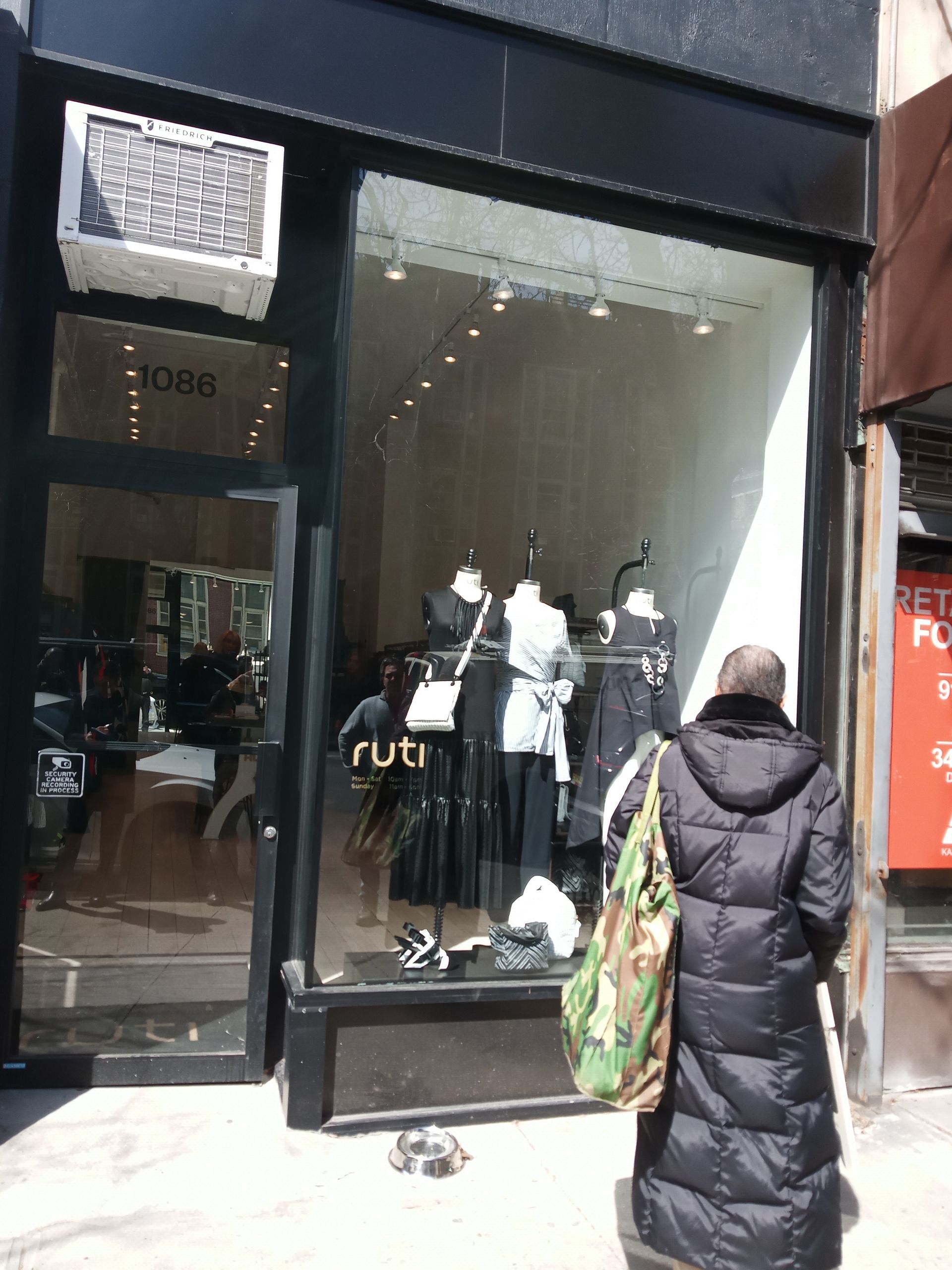 Storefront with mannequins in a large window, black exterior, and a person walking past with a patterned tote bag.
