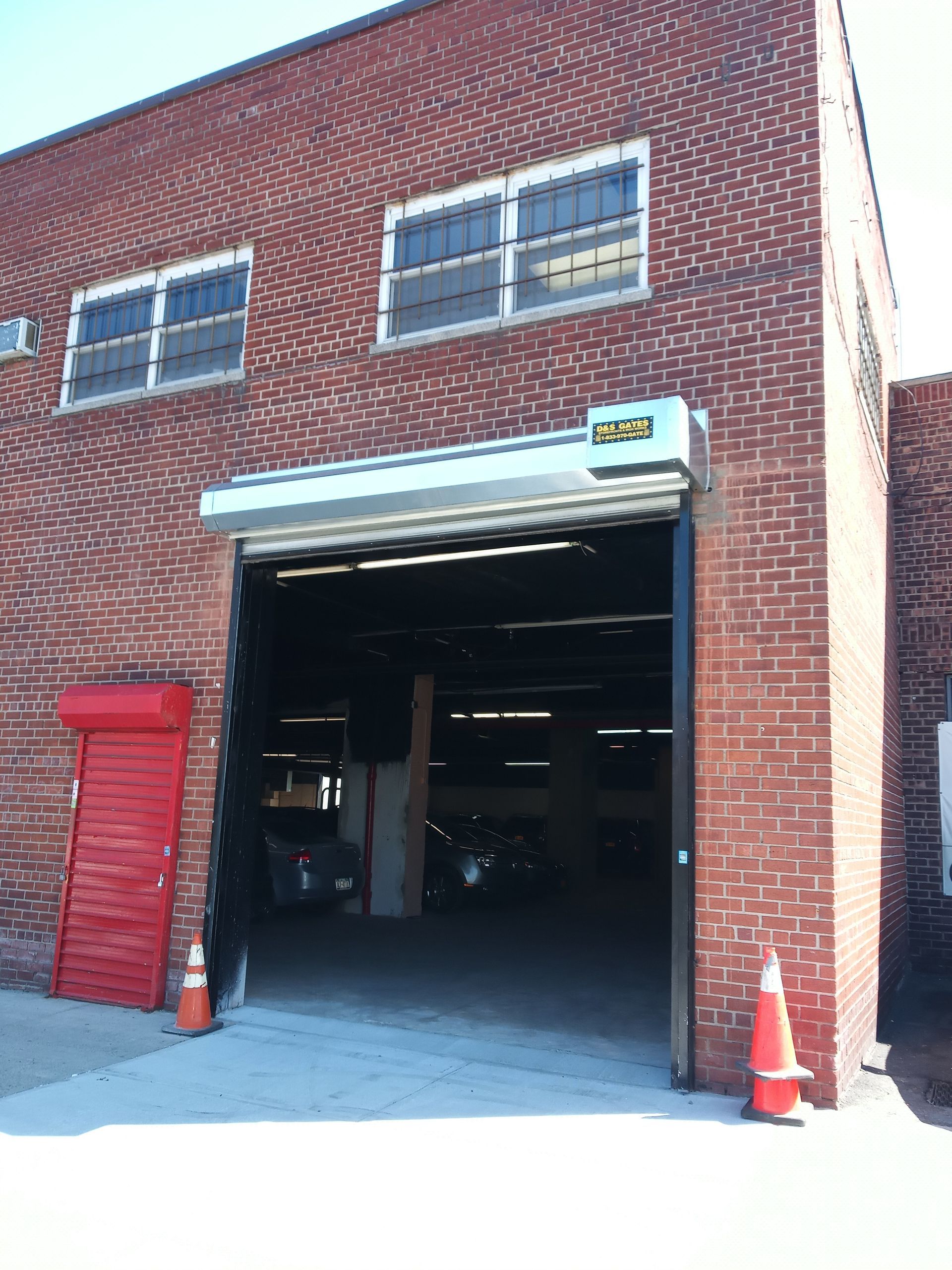 Brick building with open garage bay, red side door, and orange traffic cone outside