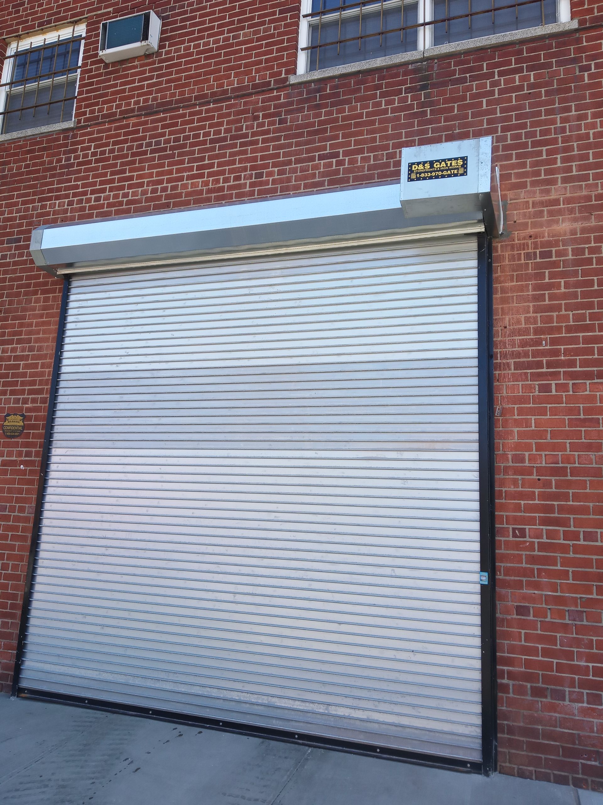 Brick building with a closed silver roll-up garage door and a small sign above it