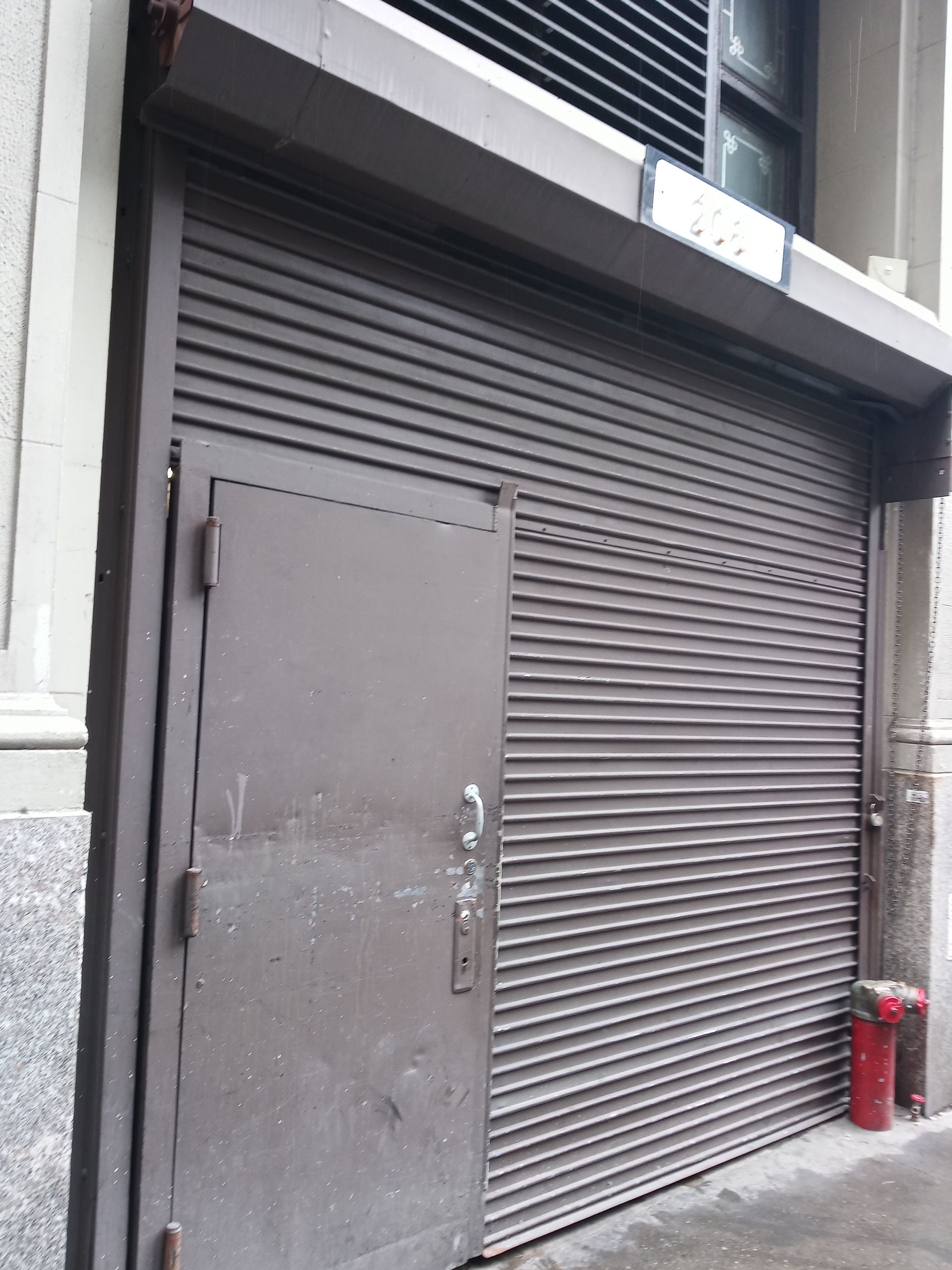Closed gray metal roll-up storefront door with a smaller side door and a red fire extinguisher nearby