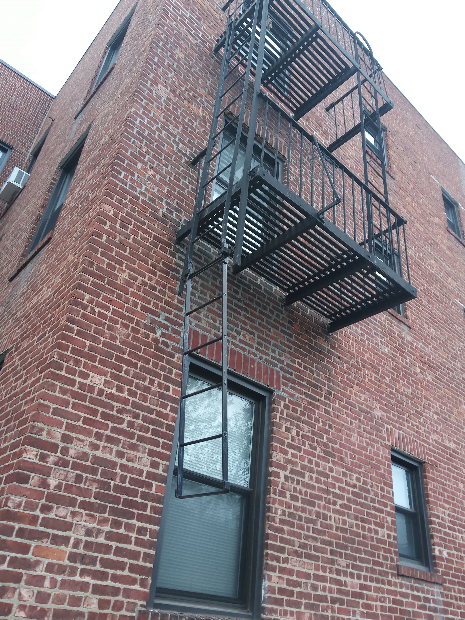 Brick building exterior with black metal fire escape and windows viewed from below