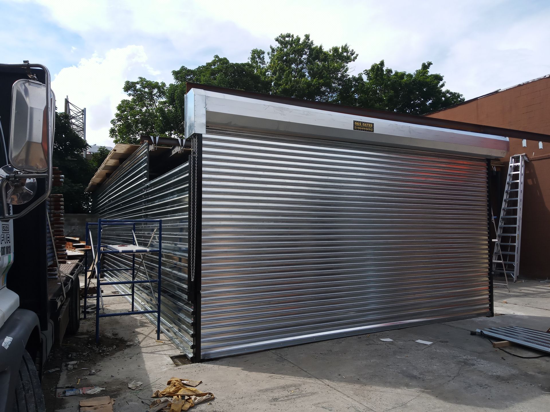 Large silver metal gate being installed at a driveway beside a truck and house
