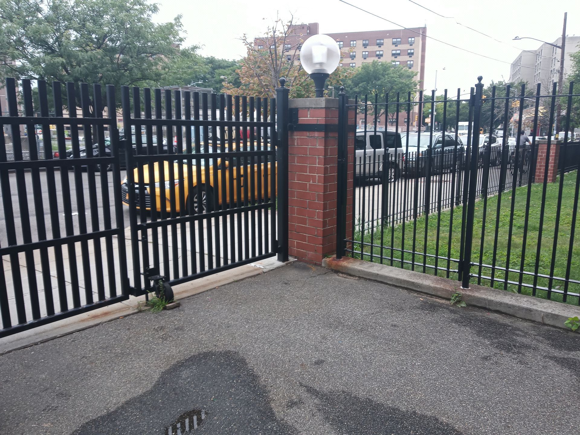 Black metal gate and brick pillars at an entrance beside a paved driveway and grass.