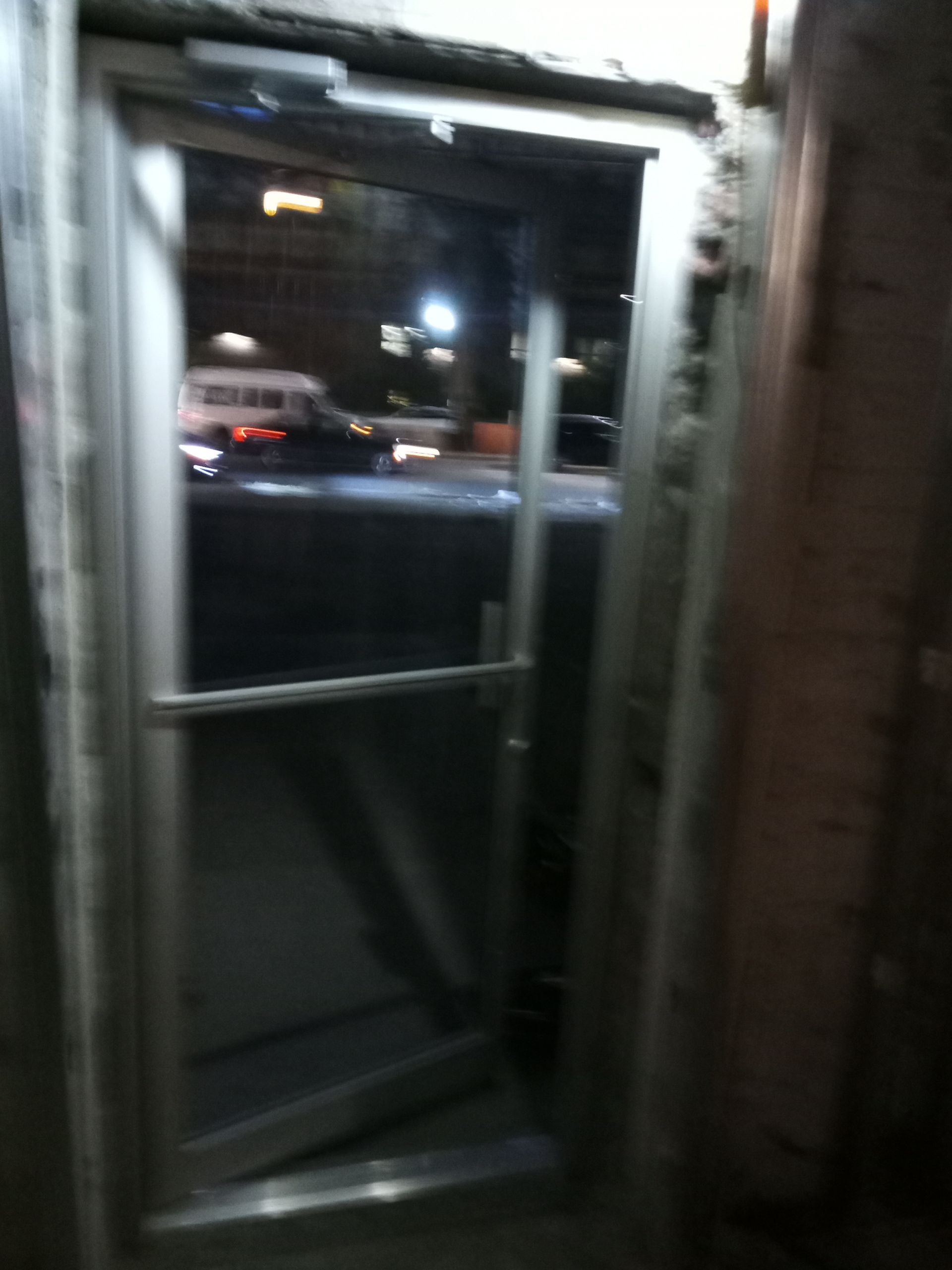 Open glass door at night with street lights and a blurred car outside